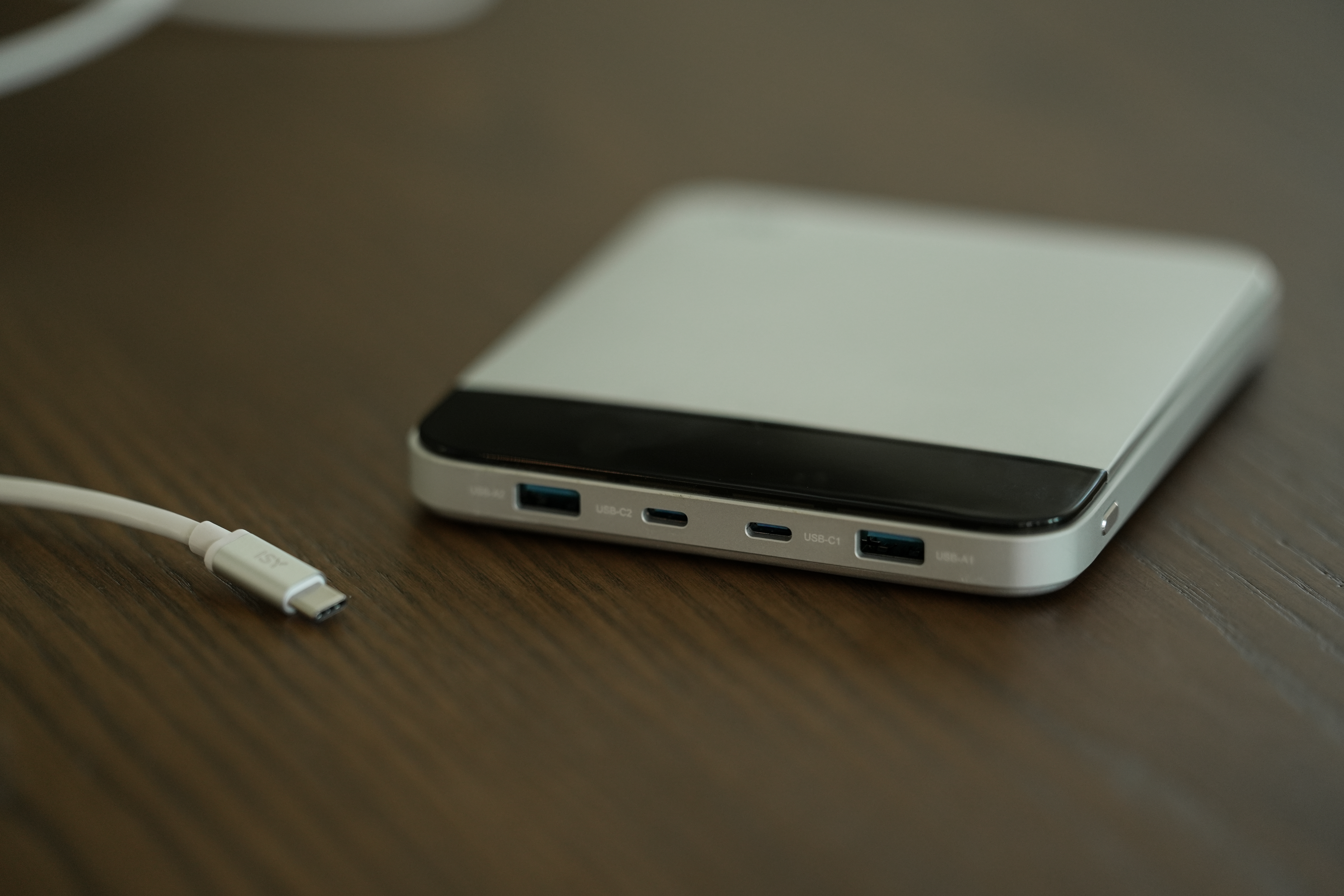 Eine silber-schwarze Powerbank mit USB-Anschlüssen. Links befindet sich ein weißes USB-C-Kabel. Die Oberfläche ist Holz.