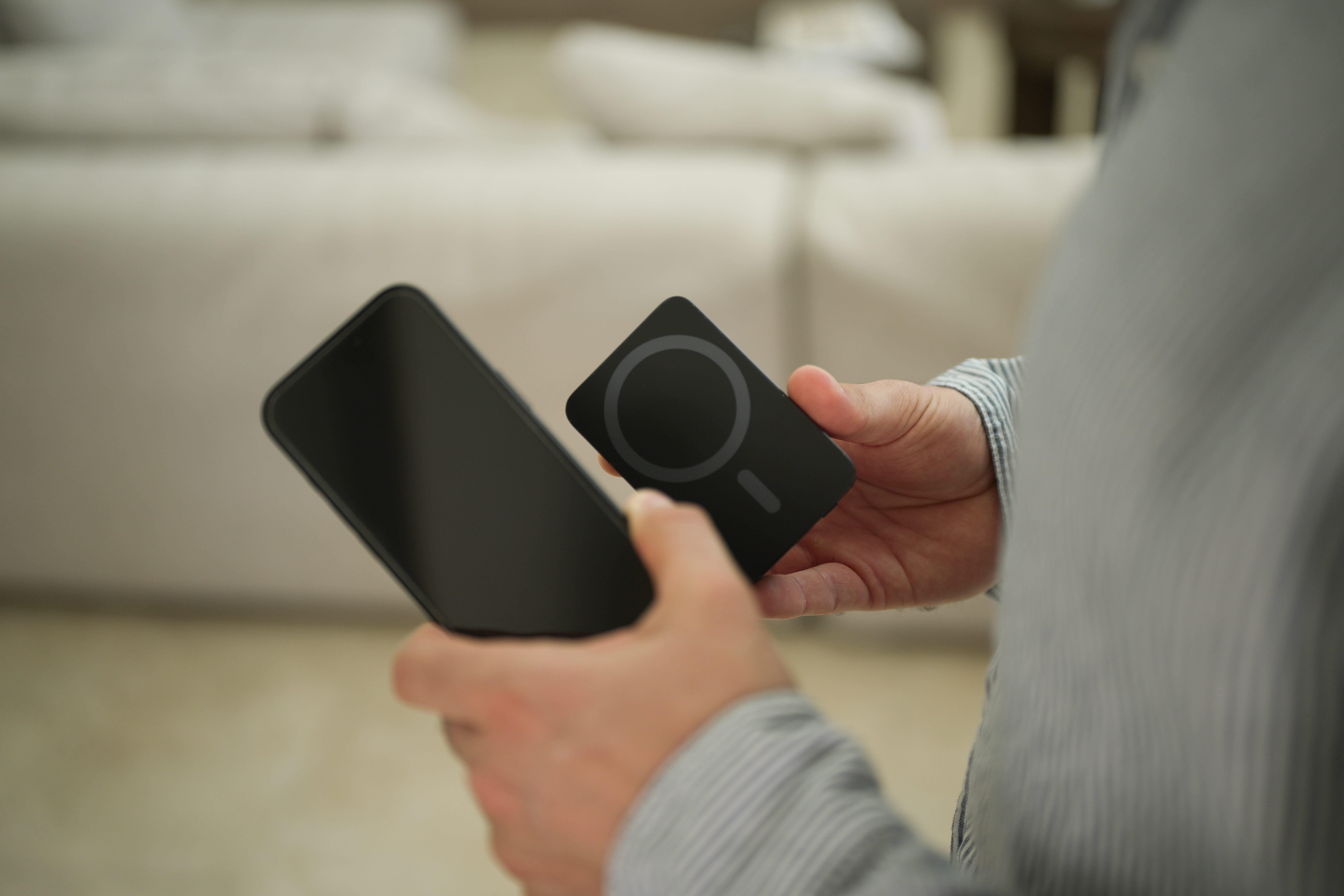 Eine Person hält ein schwarzes Smartphone und ein schwarzes MagSafe-Ladegerät. Der Hintergrund ist unscharf.