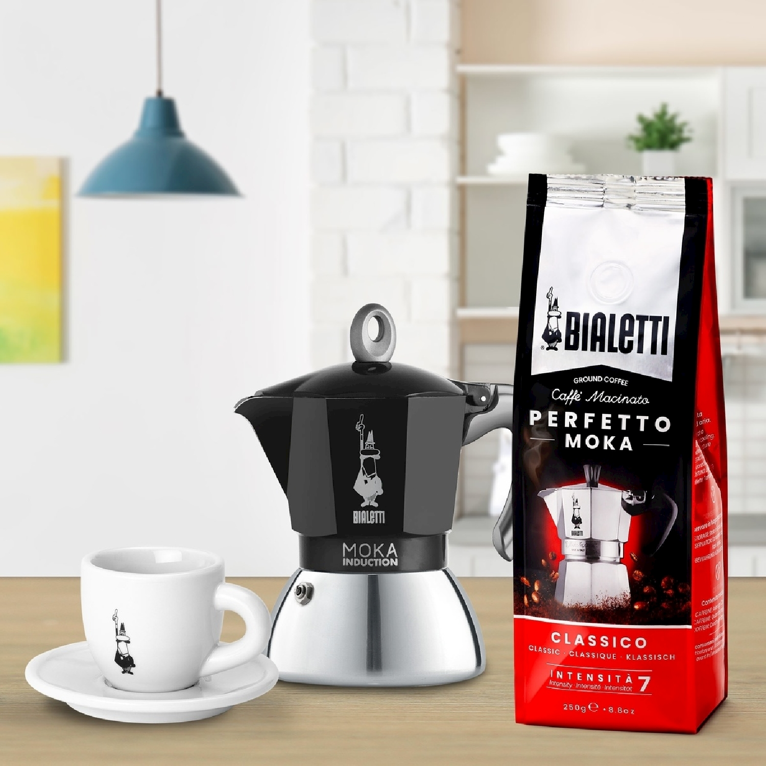 Un'attrezzatura per il caffè: caffettiera Bialetti Moka, tazza da caffè e sacchetto di caffè su un tavolo di legno. Lo sfondo include una lampada e una cucina.