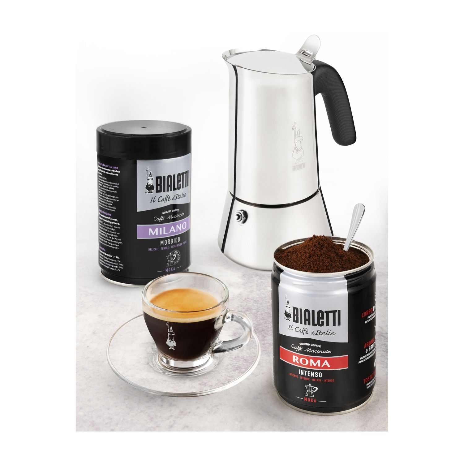 Un set di caffè con moka Bialetti, lattine di caffè e una tazzina di espresso su bianco.