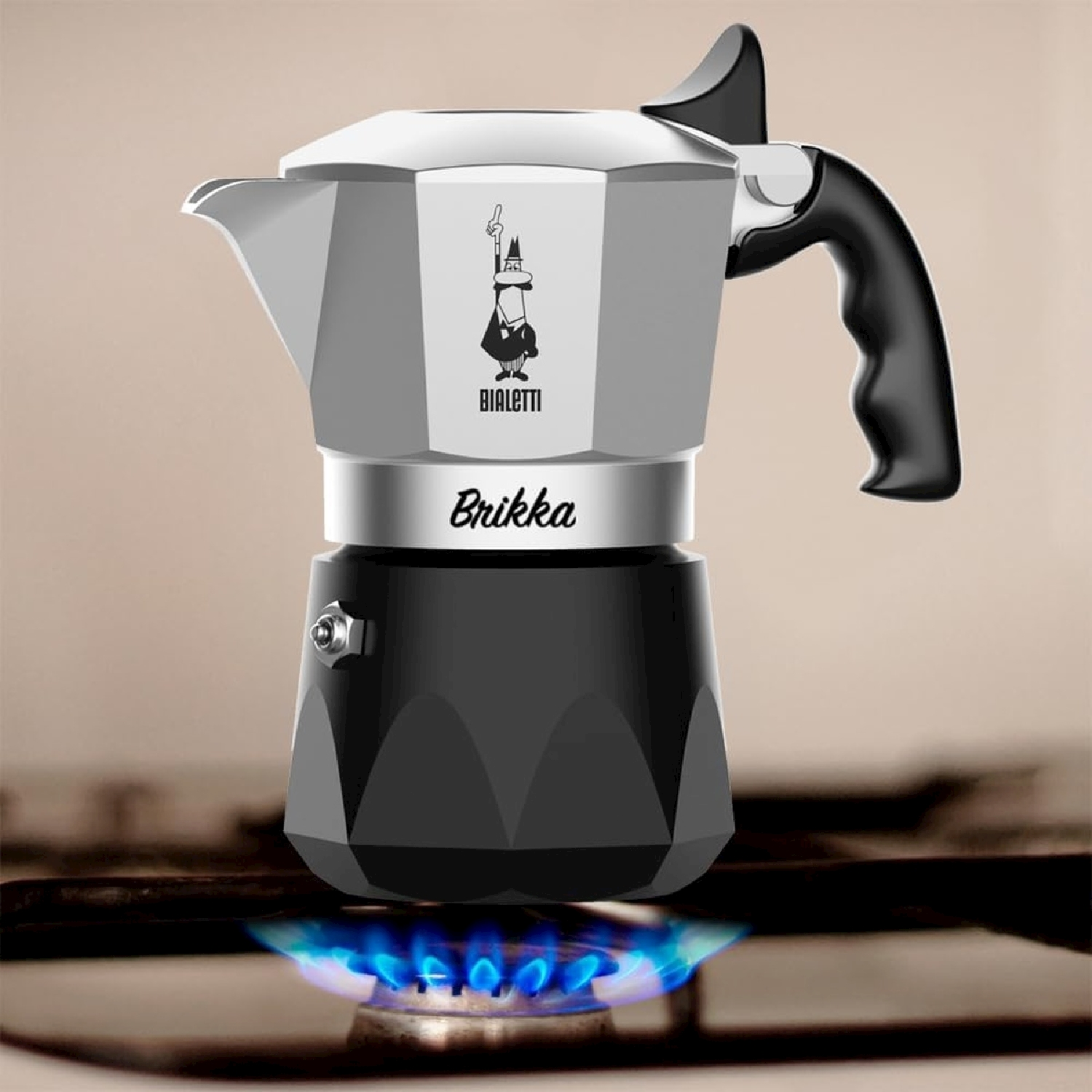 Una caffettiera Bialetti Brikka è su un fornello a gas con fiamme blu. La caffettiera è argentata e nera.