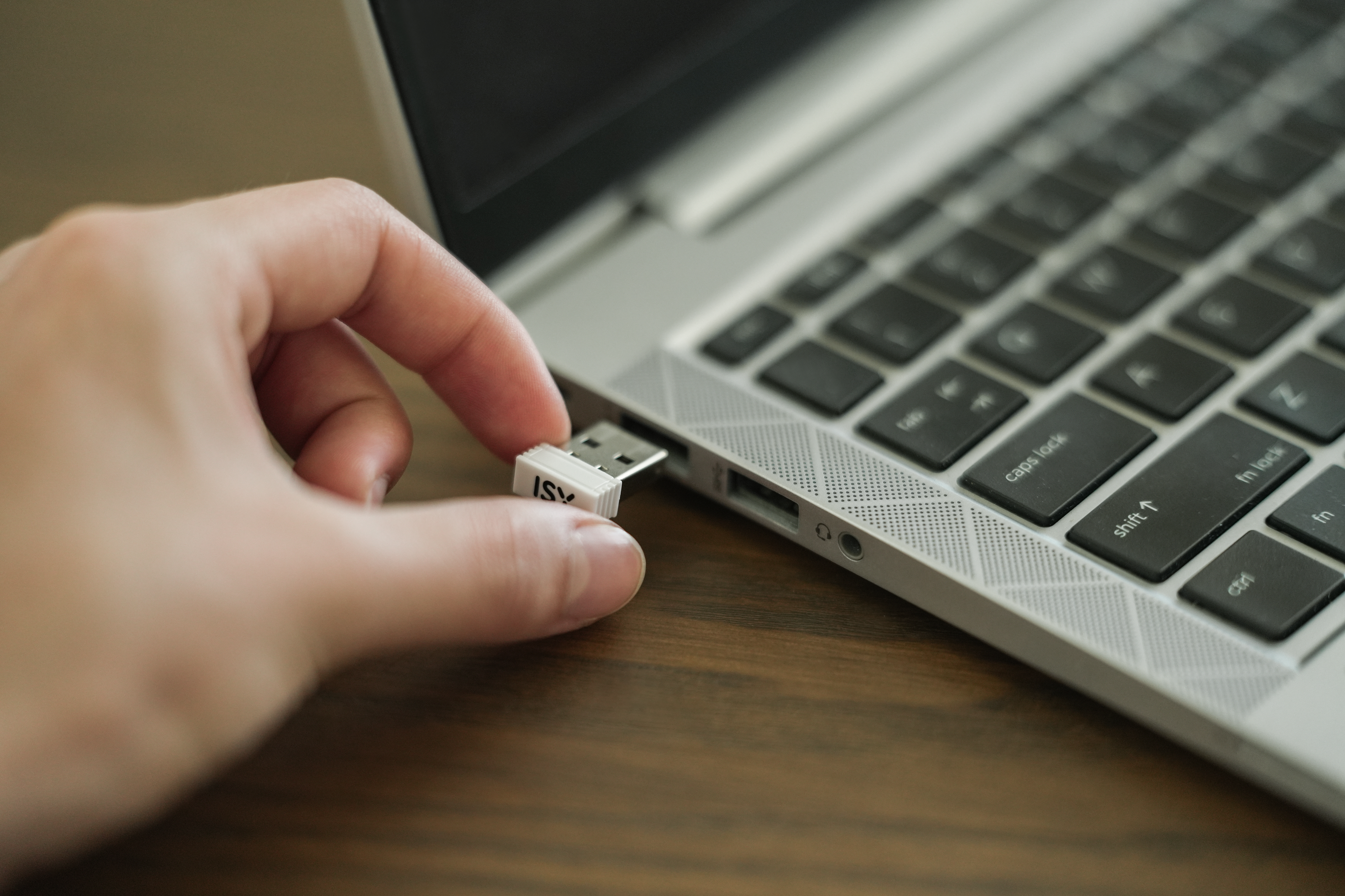 Eine Hand steckt einen weißen USB-Stick in einen Laptop. Der Laptop ist silber und hat eine schwarze Tastatur.