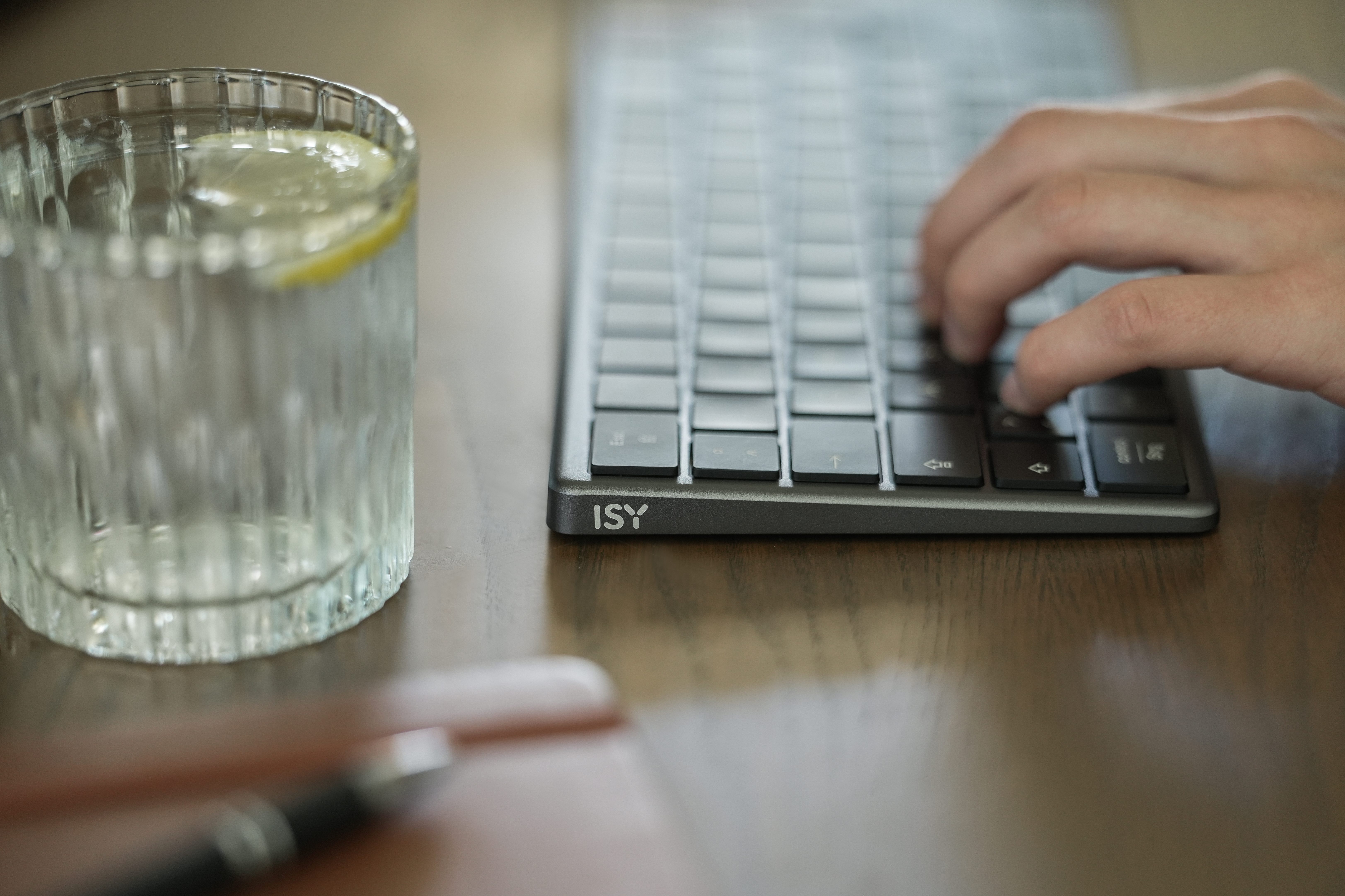Eine Hand tippt auf einer Tastatur. Daneben steht ein Glas Wasser mit Zitrone.