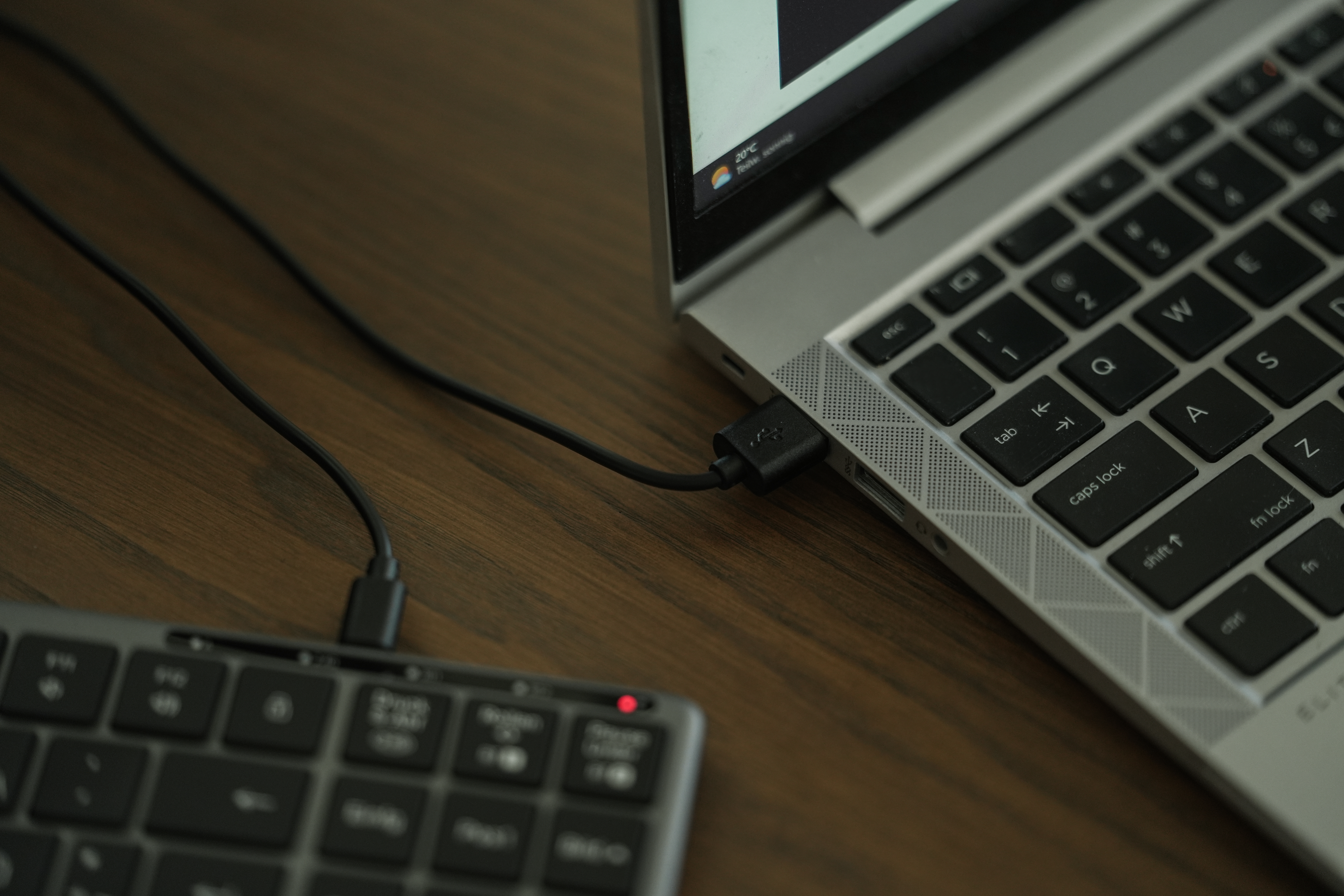 Laptop mit Tastatur über USB-Kabel verbunden. Die Tastatur ist im Vordergrund, der Laptop leicht unscharf.