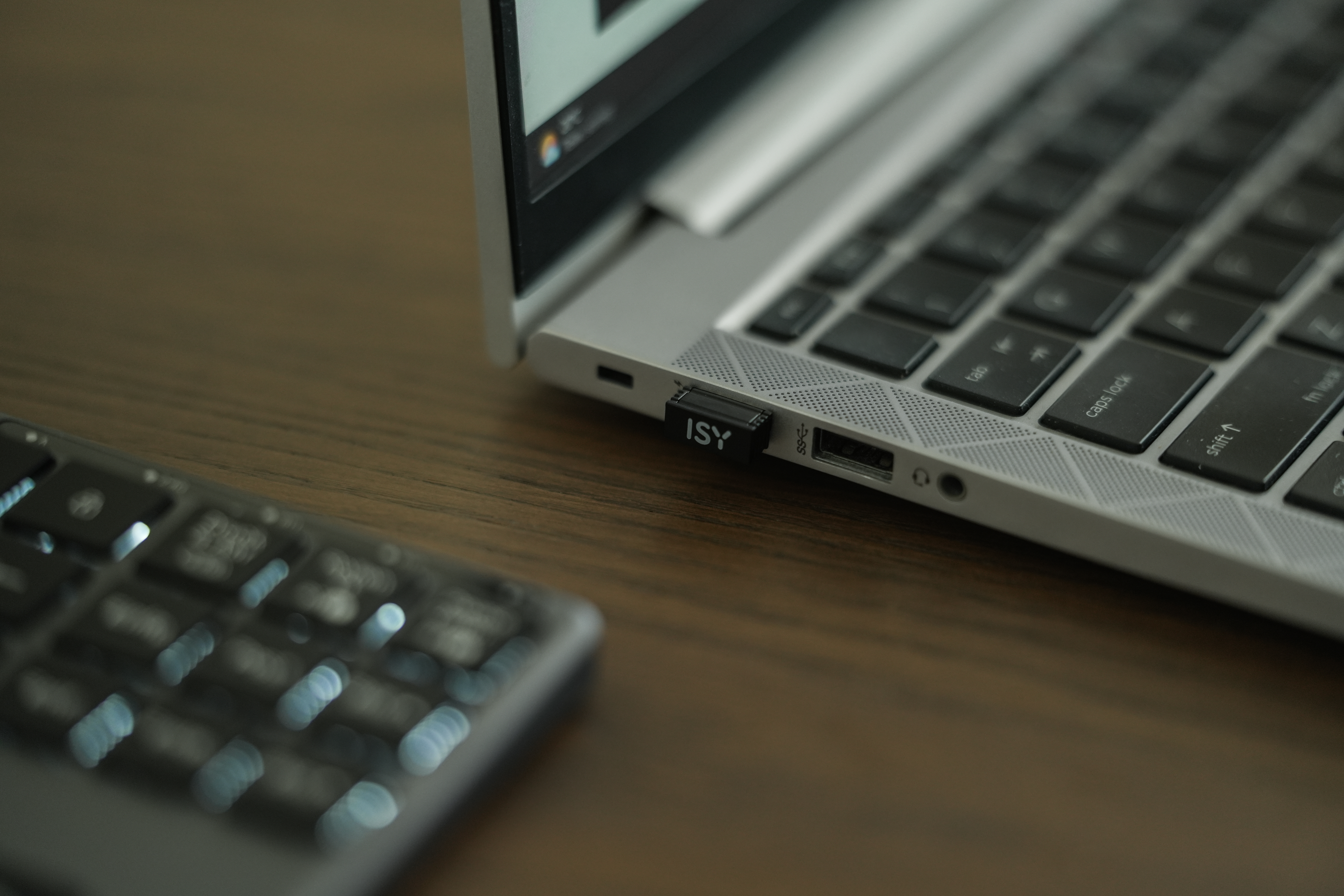 Laptop mit Tastatur, USB-Stick und separater Tastatur auf einem Holztisch. ISY-Logo auf dem USB-Stick sichtbar.