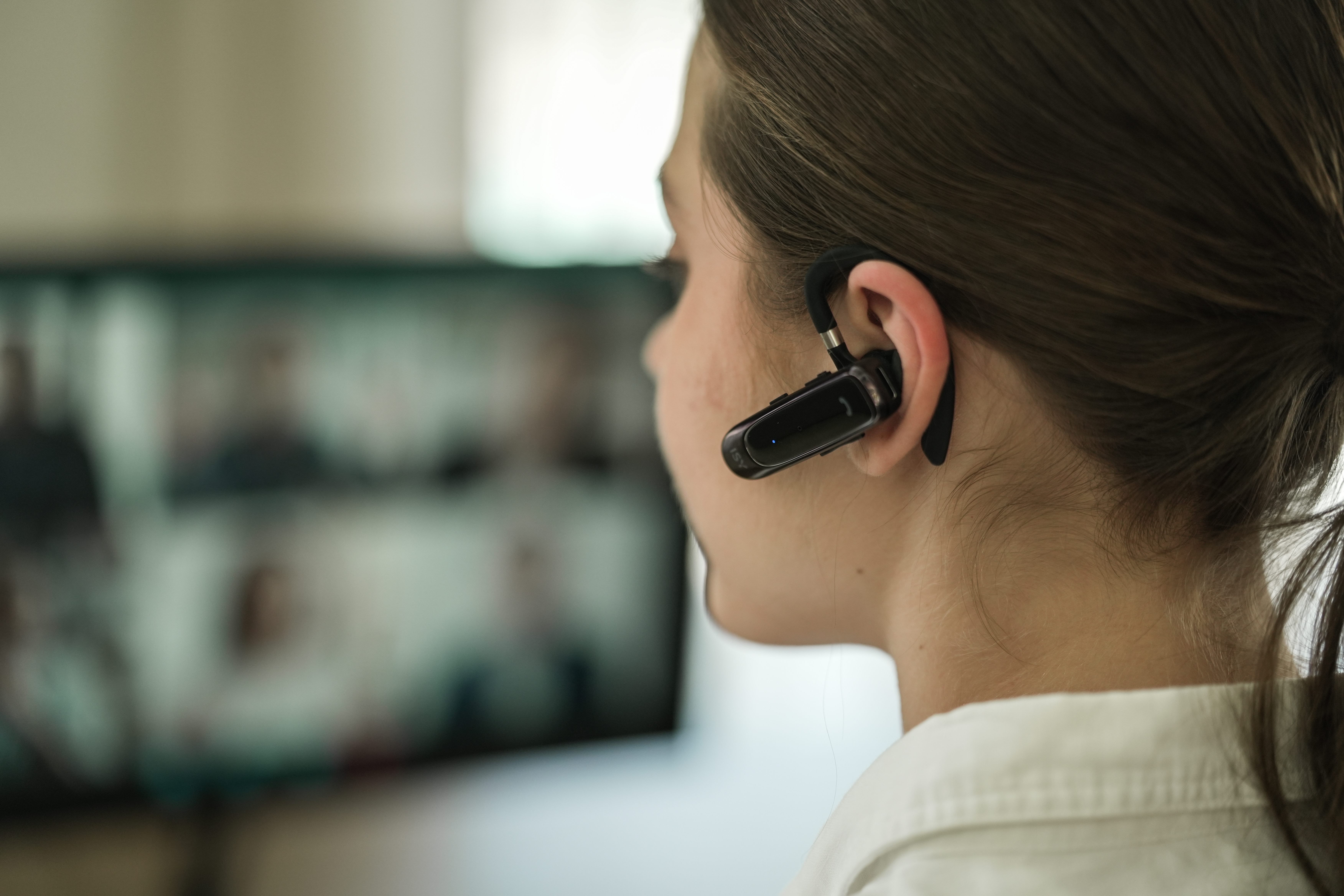 Eine Person mit Headset nimmt an einem Videoanruf teil. Die Person ist von der Kamera abgewandt. Im Hintergrund ist ein Bildschirm zu sehen.