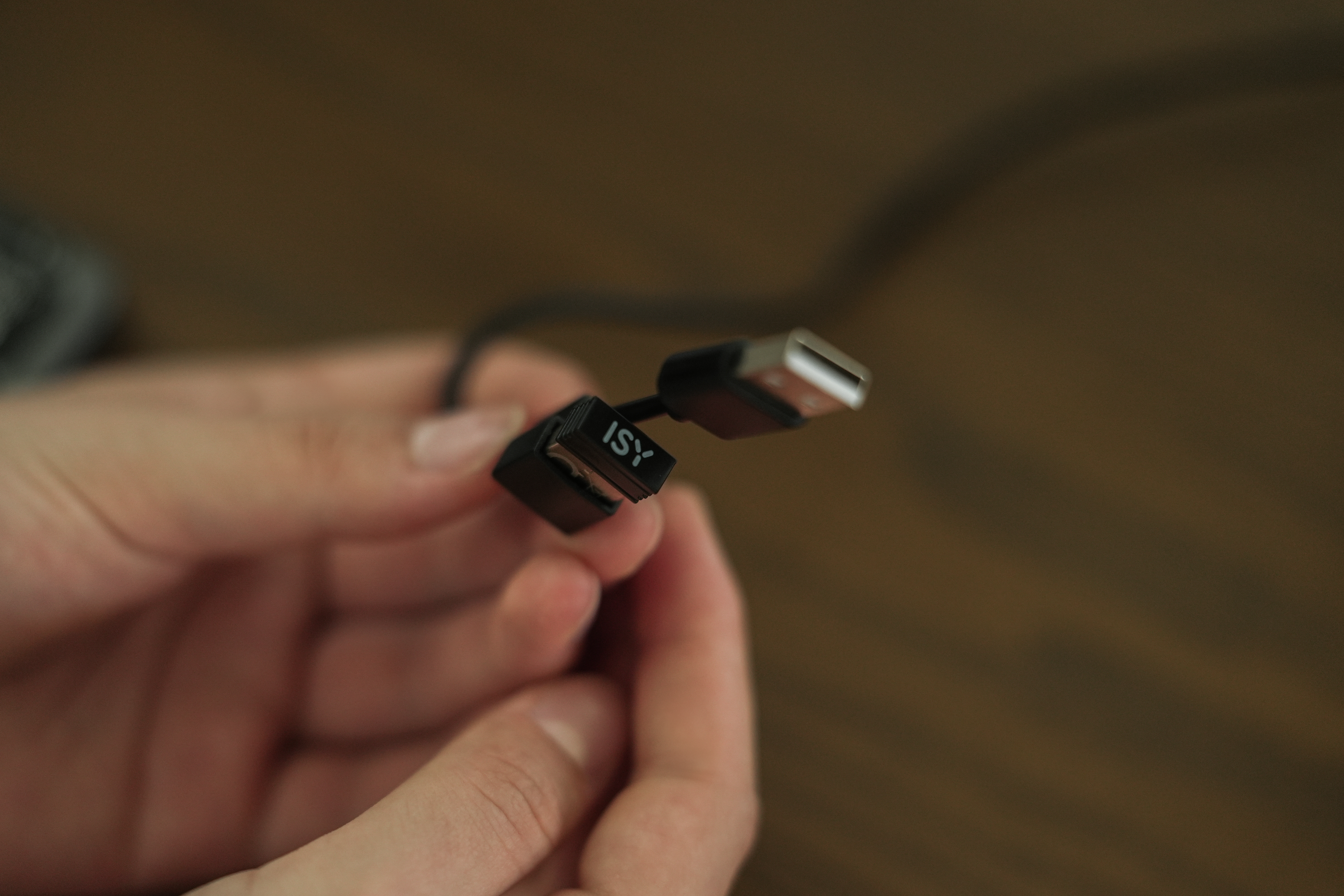 Hände halten ein schwarzes USB-Kabel mit USB-Anschluss und einem rechteckigen Stecker mit der Aufschrift ISY.
