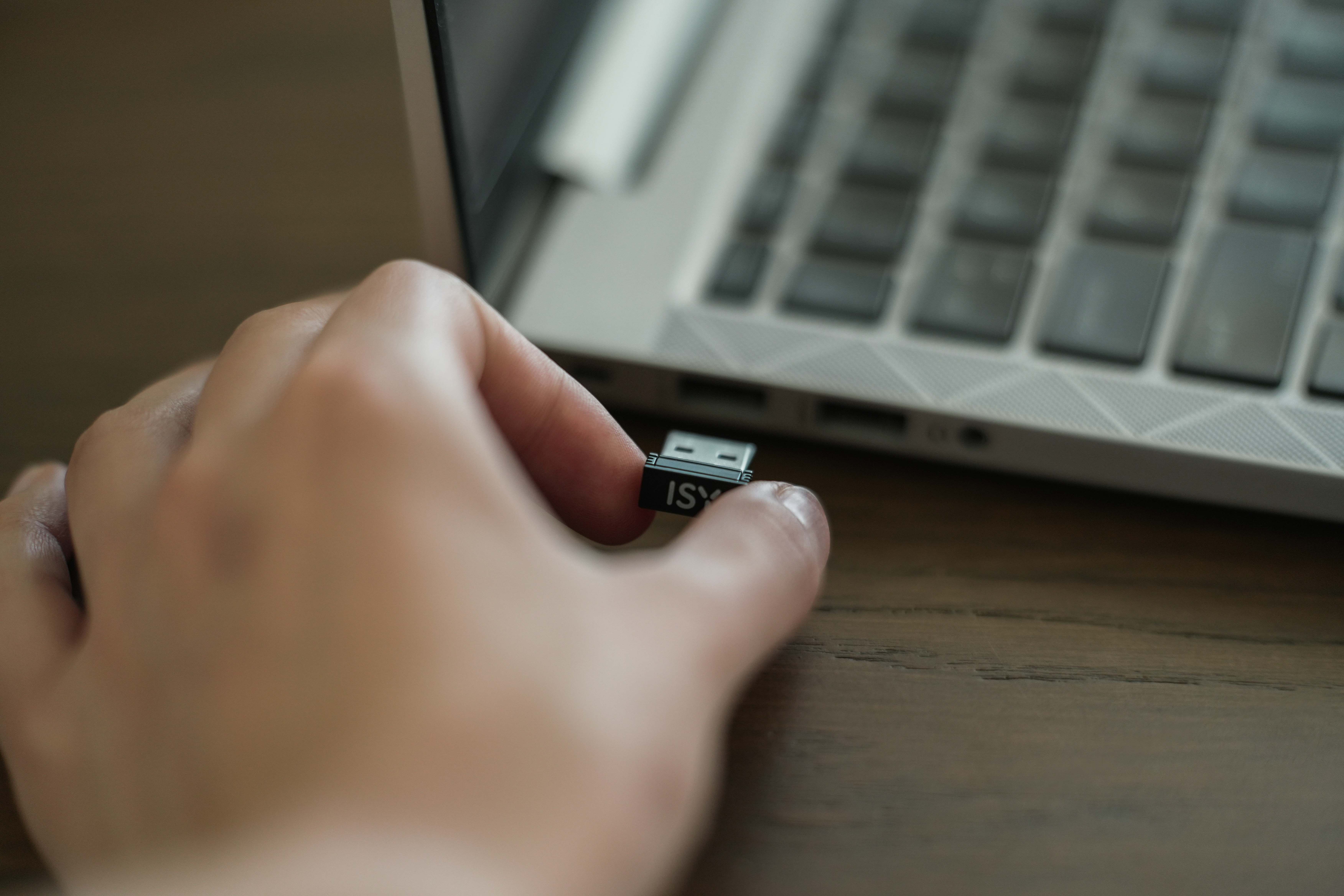 Hand führt einen schwarzen USB-Stick in einen Laptop ein. Der Laptop steht auf einem Holztisch.
