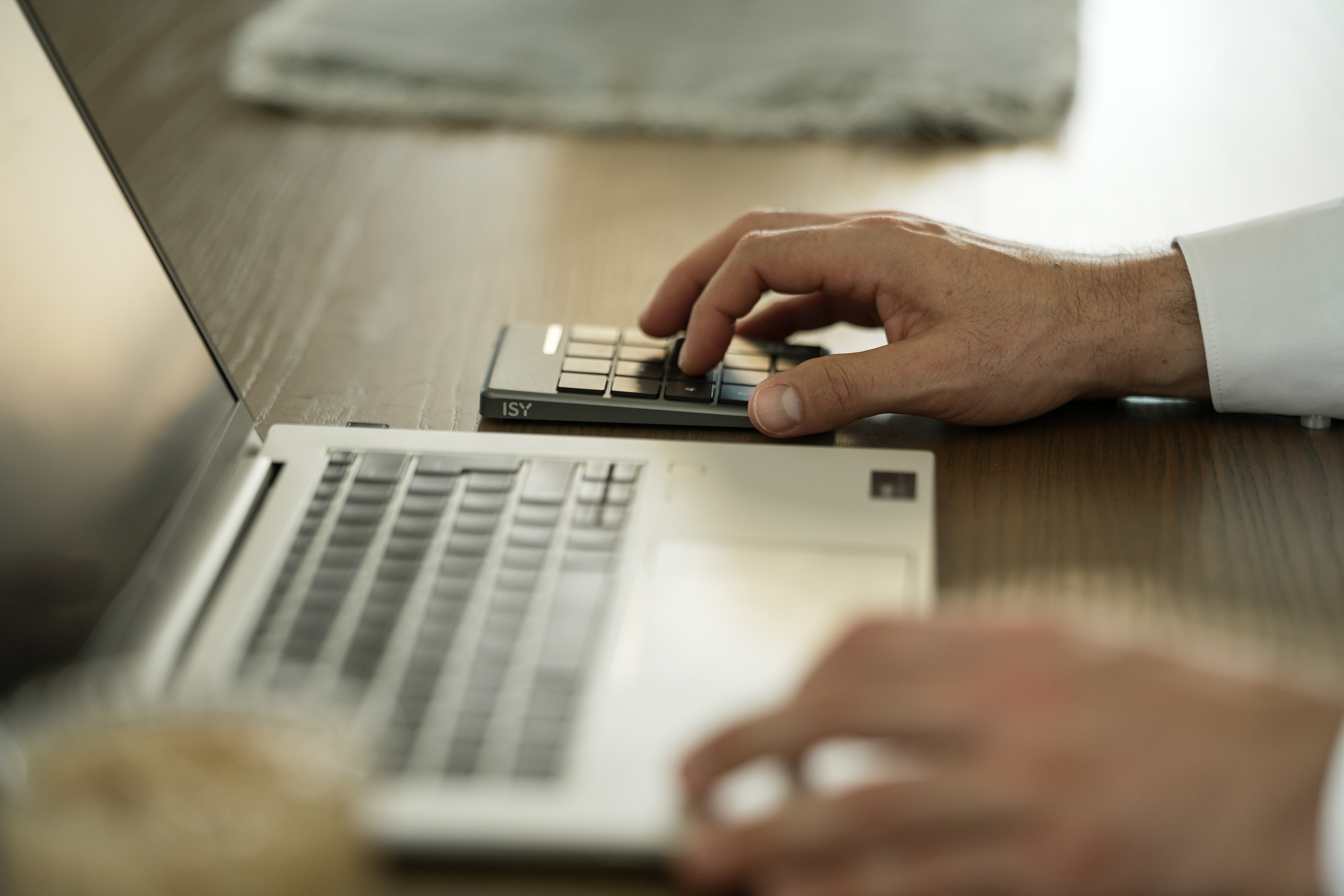 Eine Person bedient Laptop und Mini-Tastatur. Auf Holzschreibtisch mit verschwommenem Hintergrund.