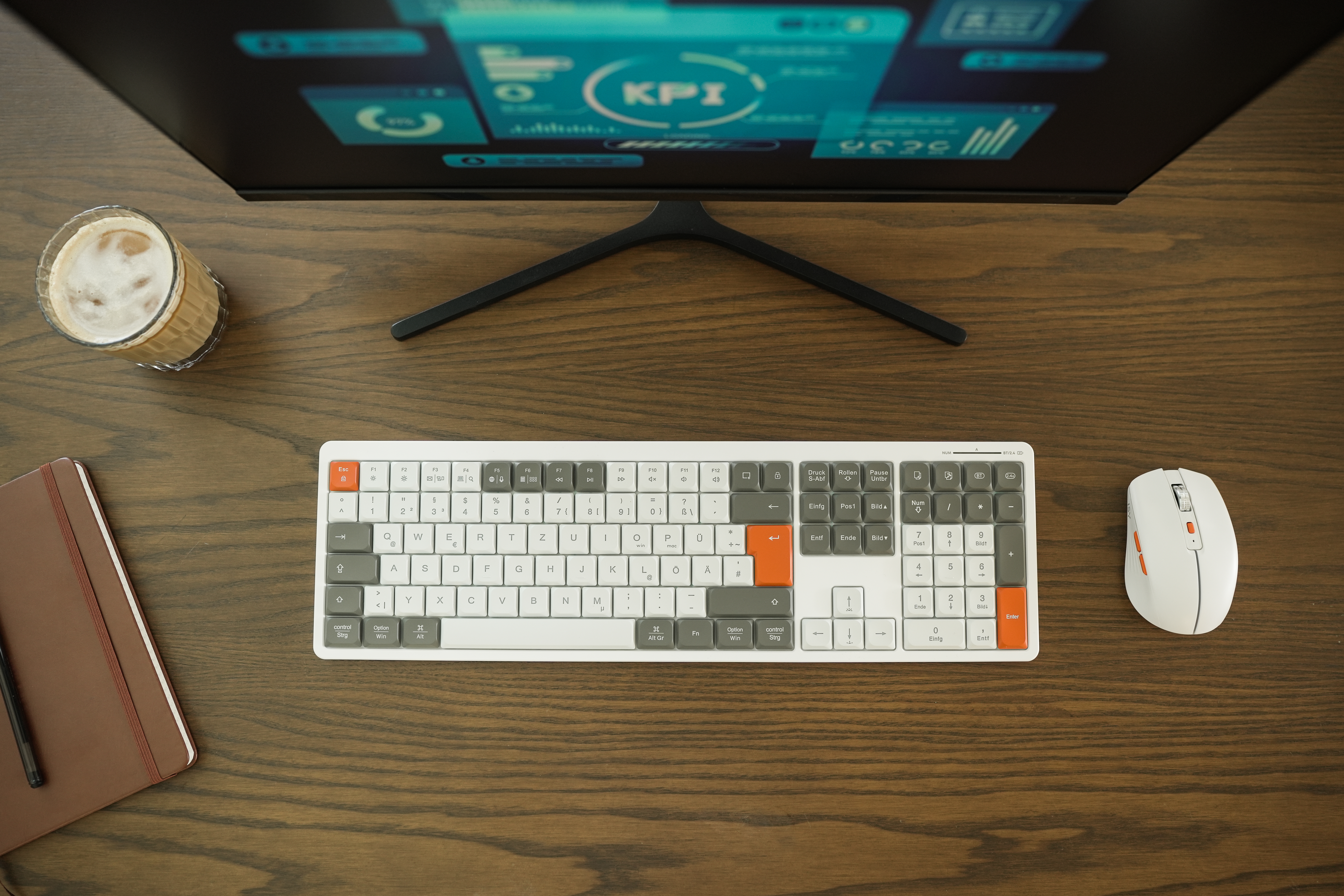 Ein Schreibtisch-Setup mit Monitor, Tastatur, Maus, Kaffee und Notizbuch.