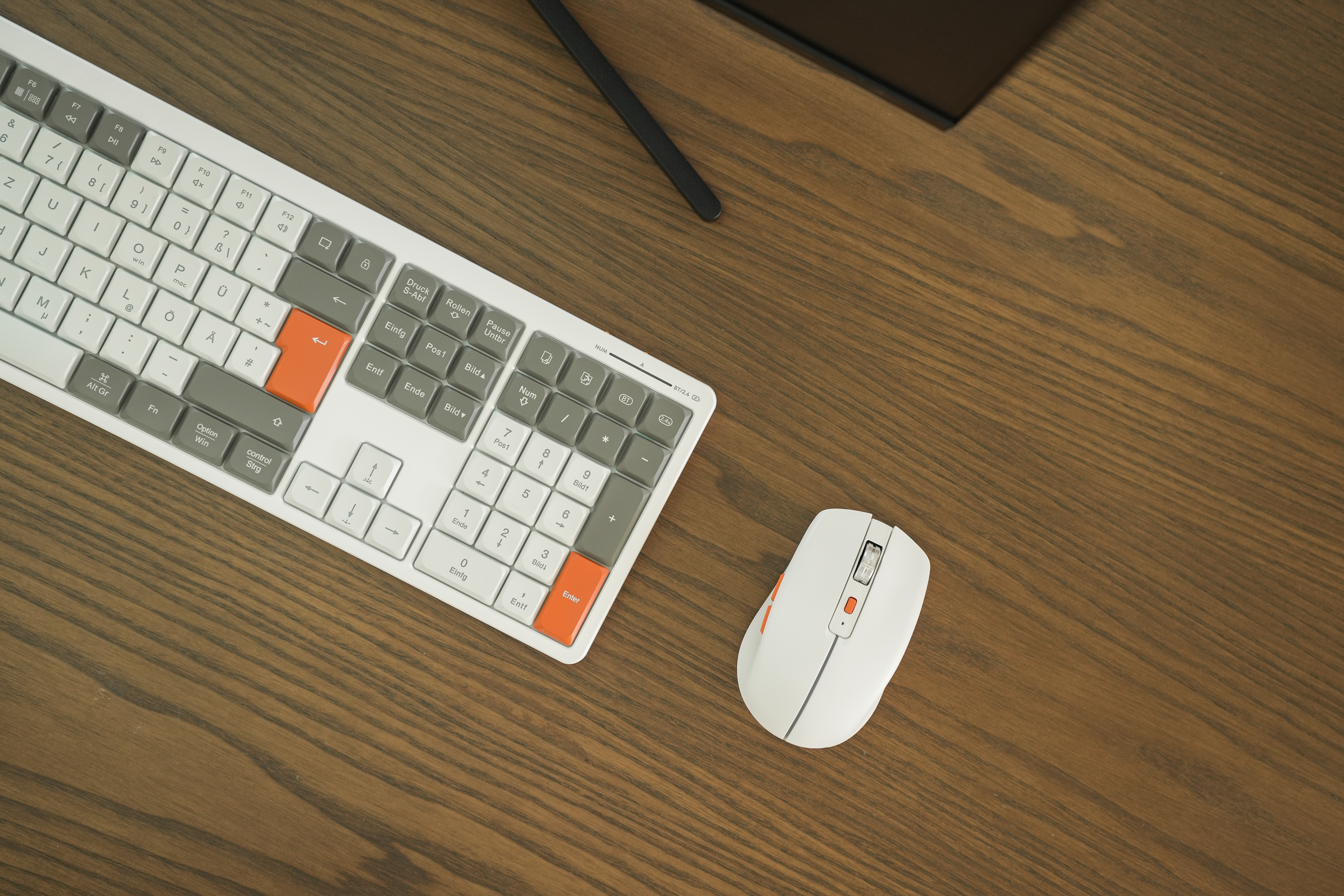 Draufsicht auf Tastatur und Maus auf einem Holzschreibtisch. Die Tastatur ist weiß, die Maus ebenfalls.