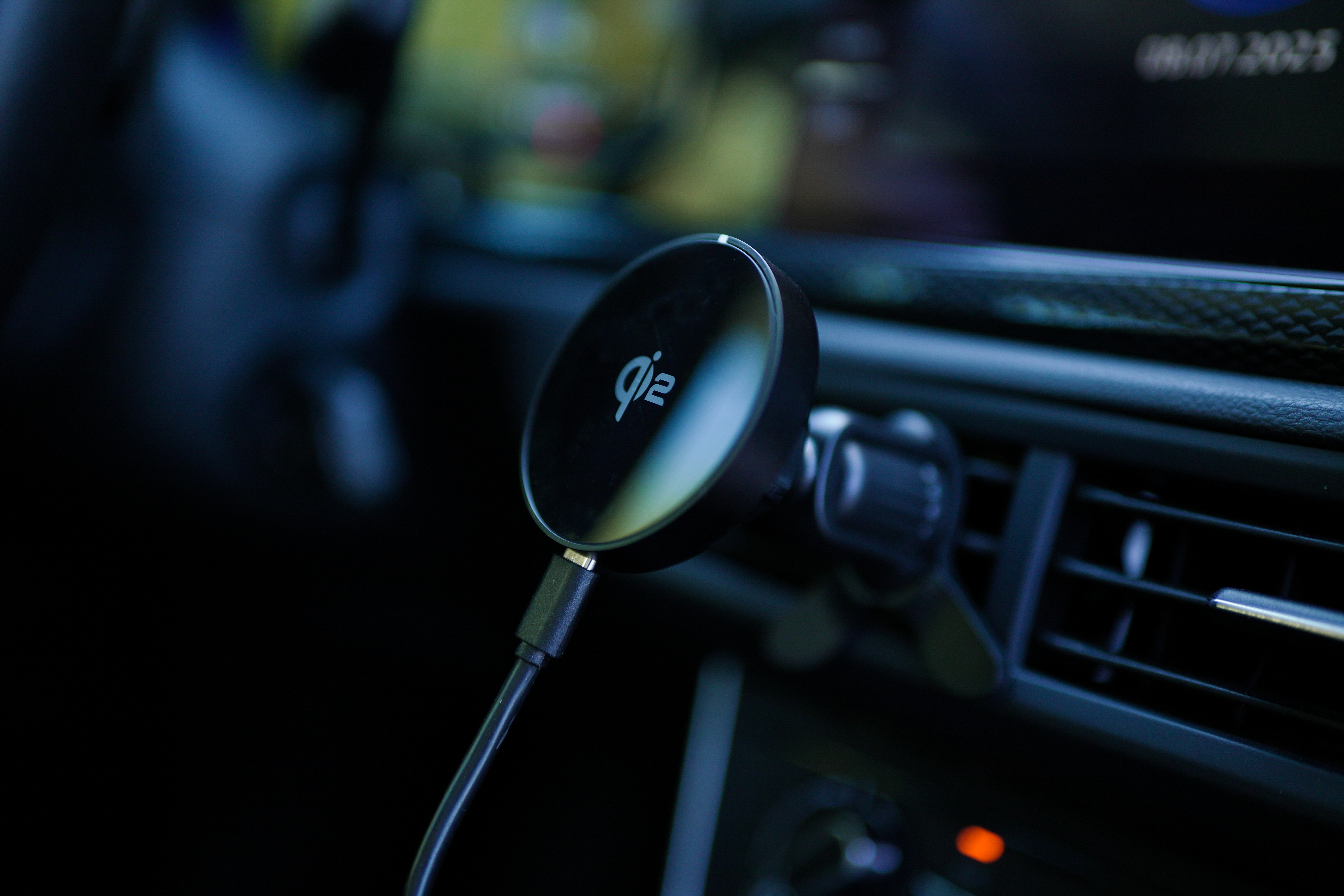 Ein Qi2-Funkladegerät ist im Auto montiert. Es ist schwarz und per Kabel verbunden. Der Hintergrund ist unscharf.