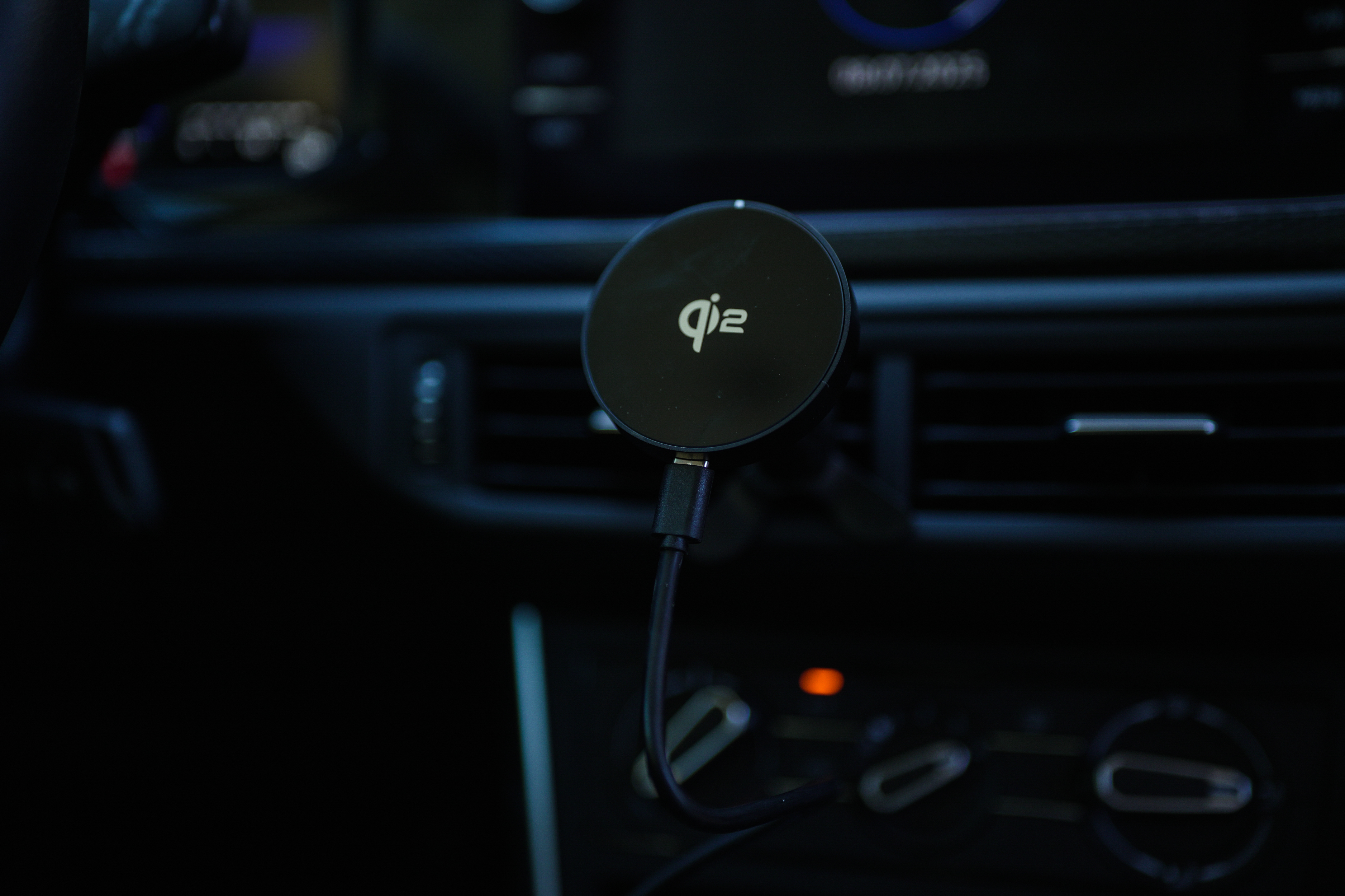 Ein schwarzes Qi-Funkladegerät ist an das Armaturenbrett eines Autos angeschlossen. Das Ladegerät hat das Qi-Logo.
