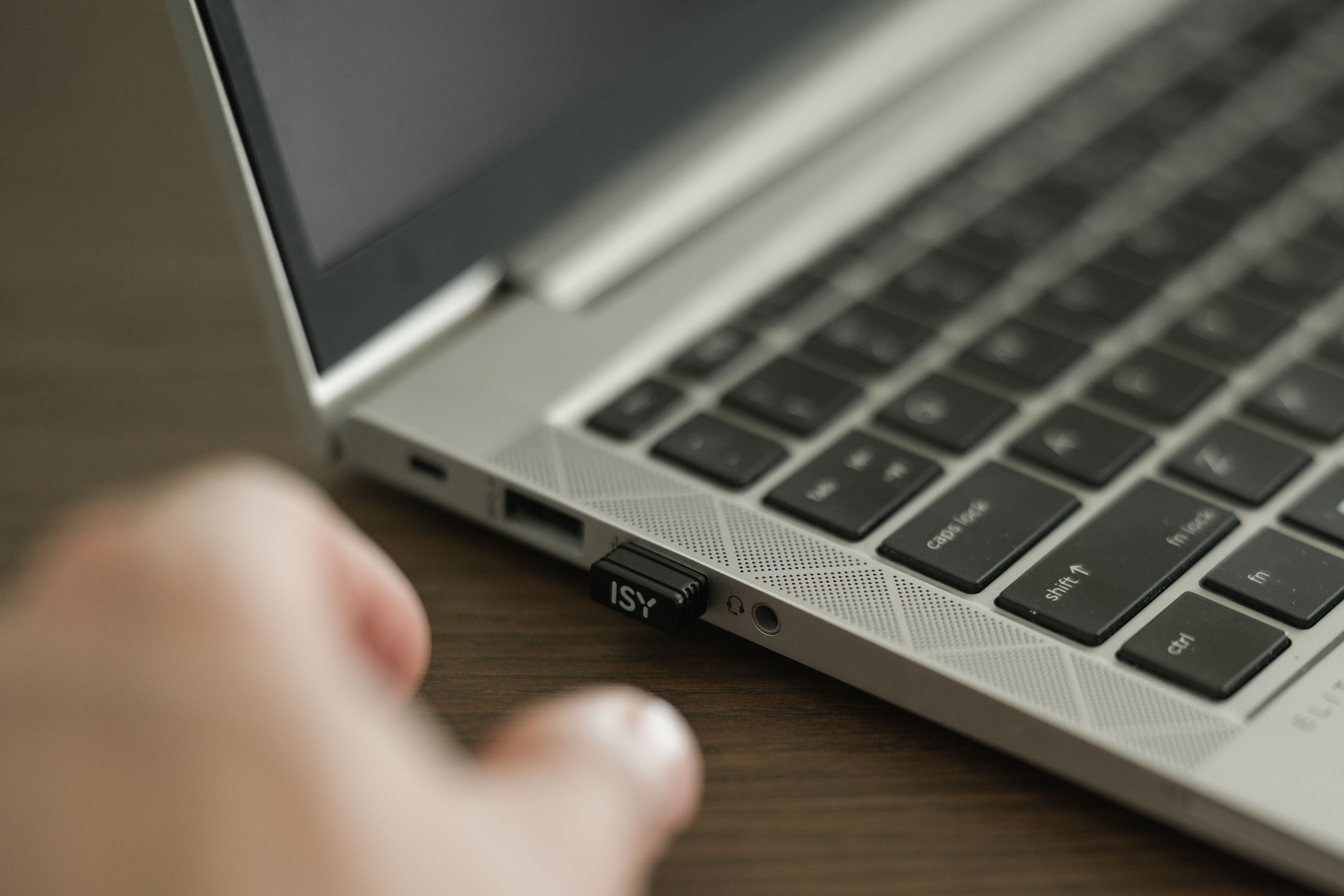 Laptop mit Tastatur und ISY-USB-Laufwerk. Hand im Vordergrund, Holztisch im Hintergrund.