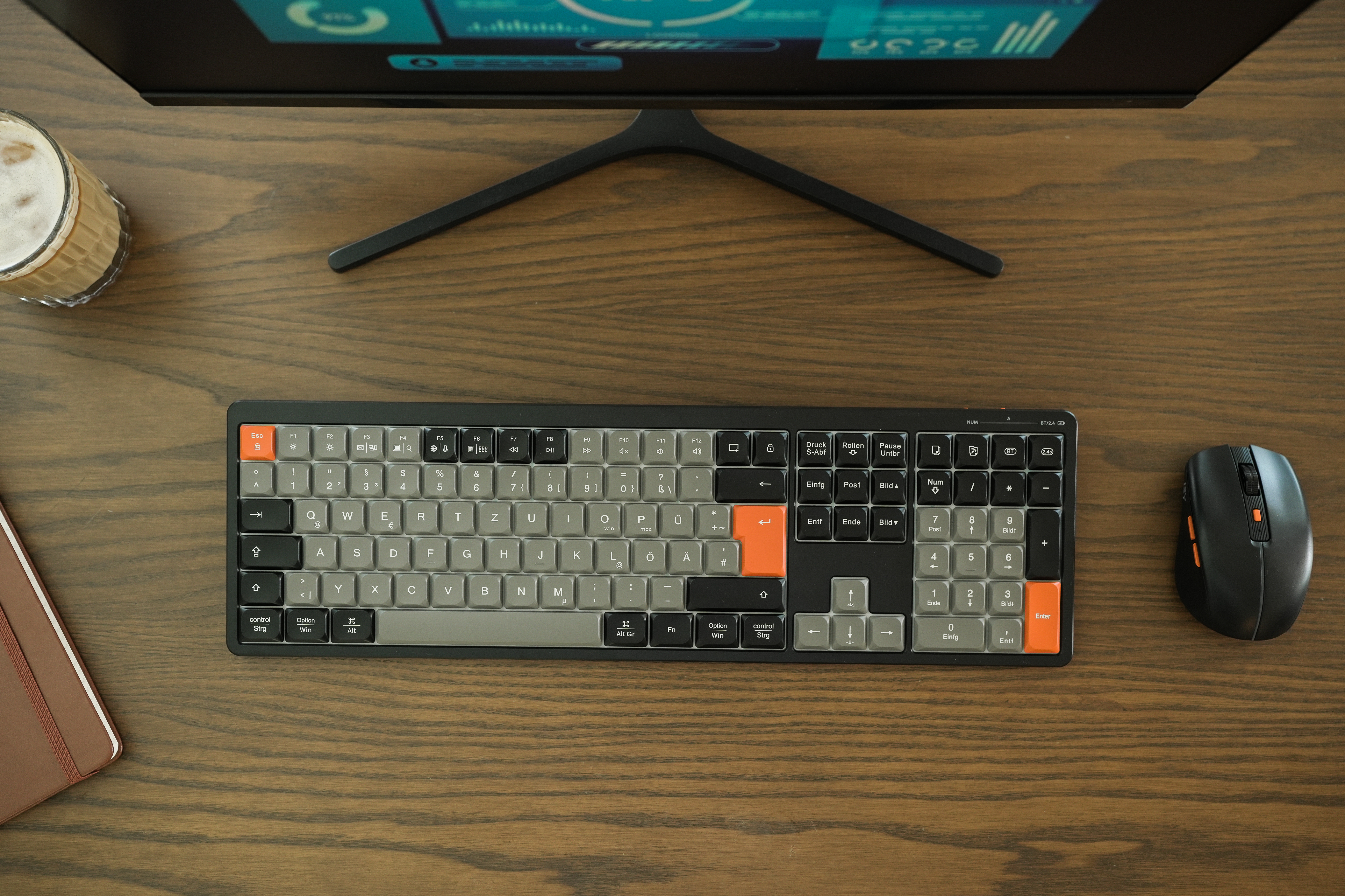 Ein Schreibtisch mit Tastatur, Maus und Monitor. Links steht ein Glas Getränk.
