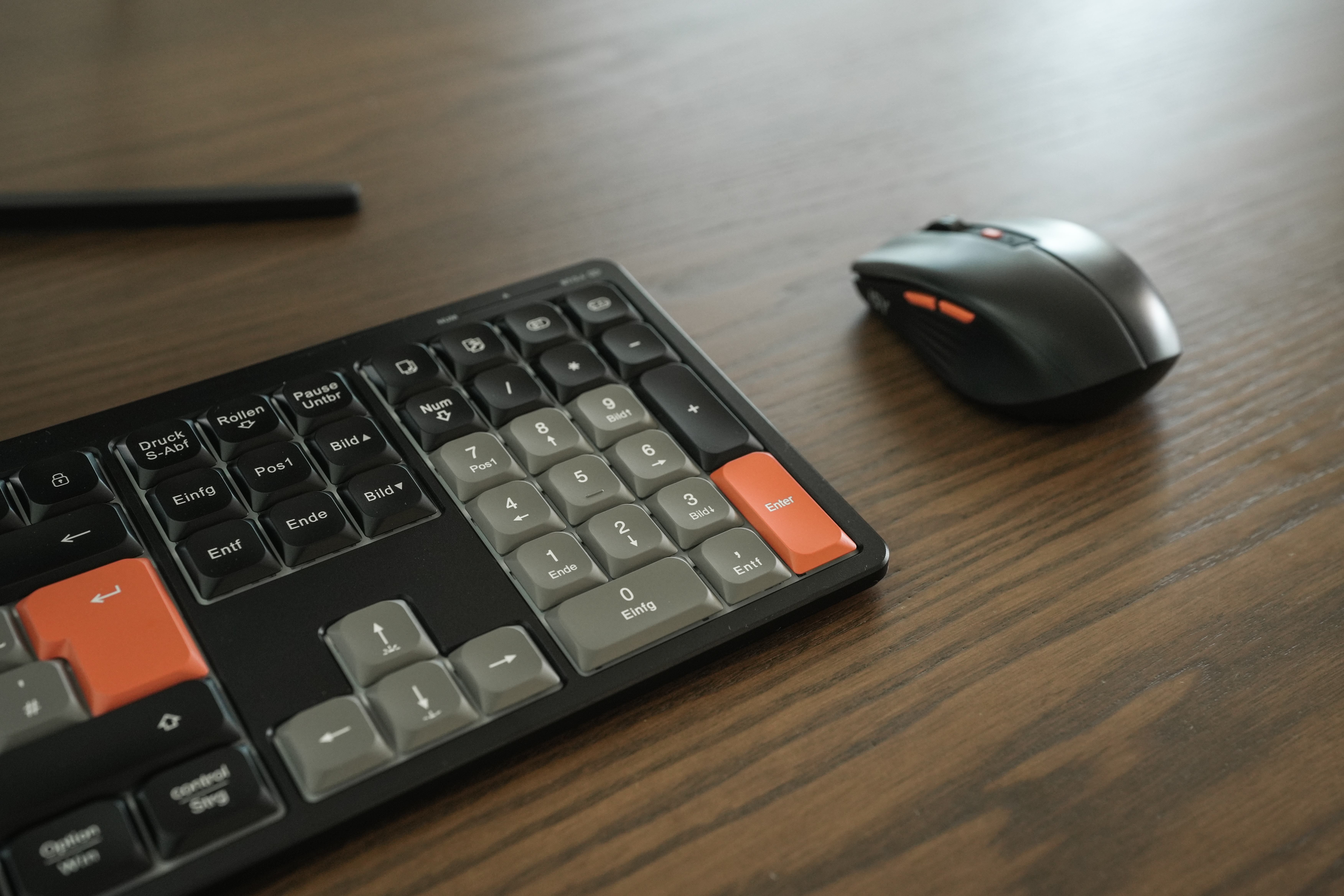 Eine Tastatur und Maus auf einem Holztisch. Die Tastatur hat schwarze Tasten mit orangefarbenen und grauen Akzenten.