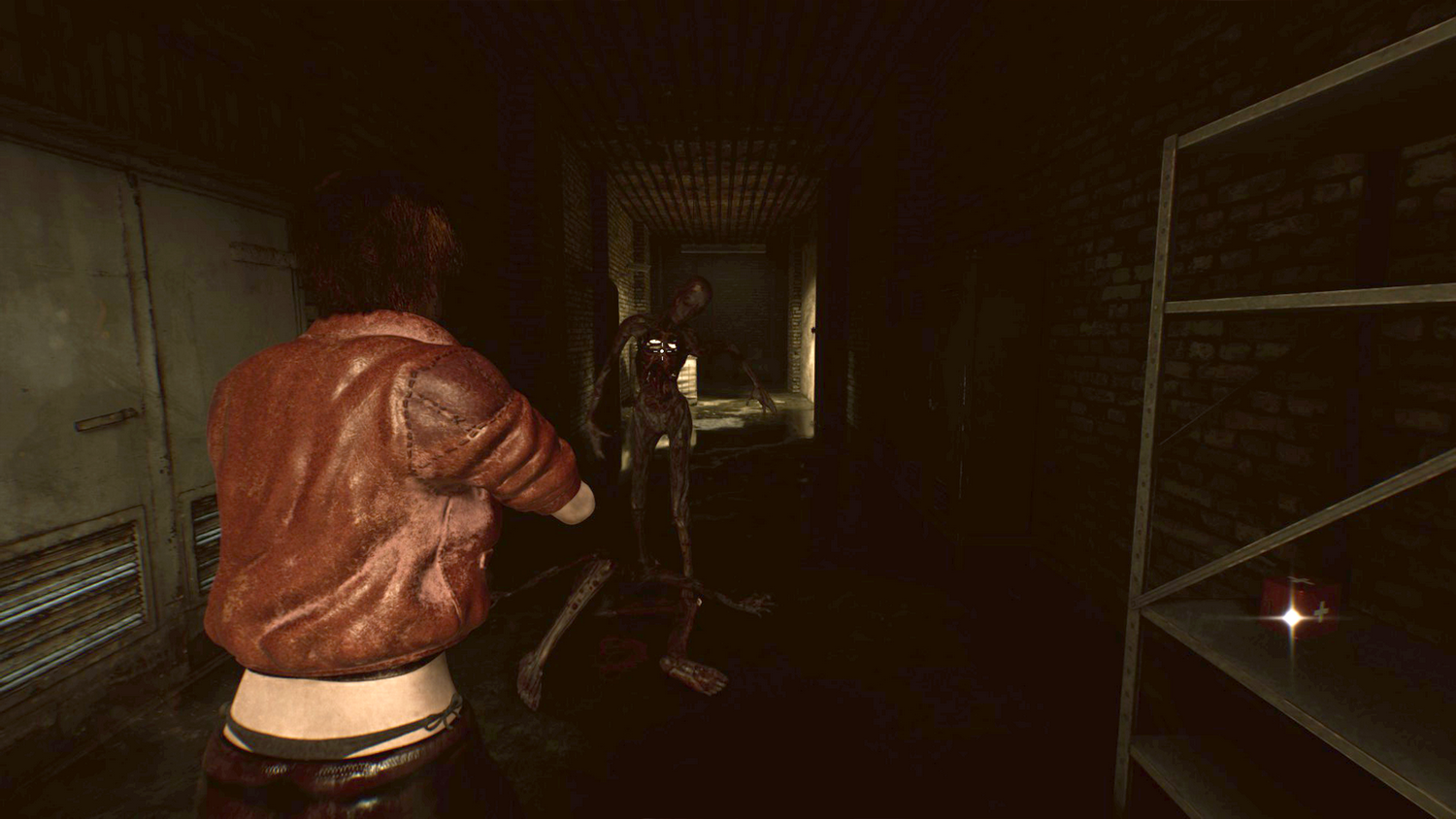 Una persona con chaqueta marrón se enfrenta a dos zombis en un pasillo oscuro. Un estante de metal con un botiquín a la derecha.