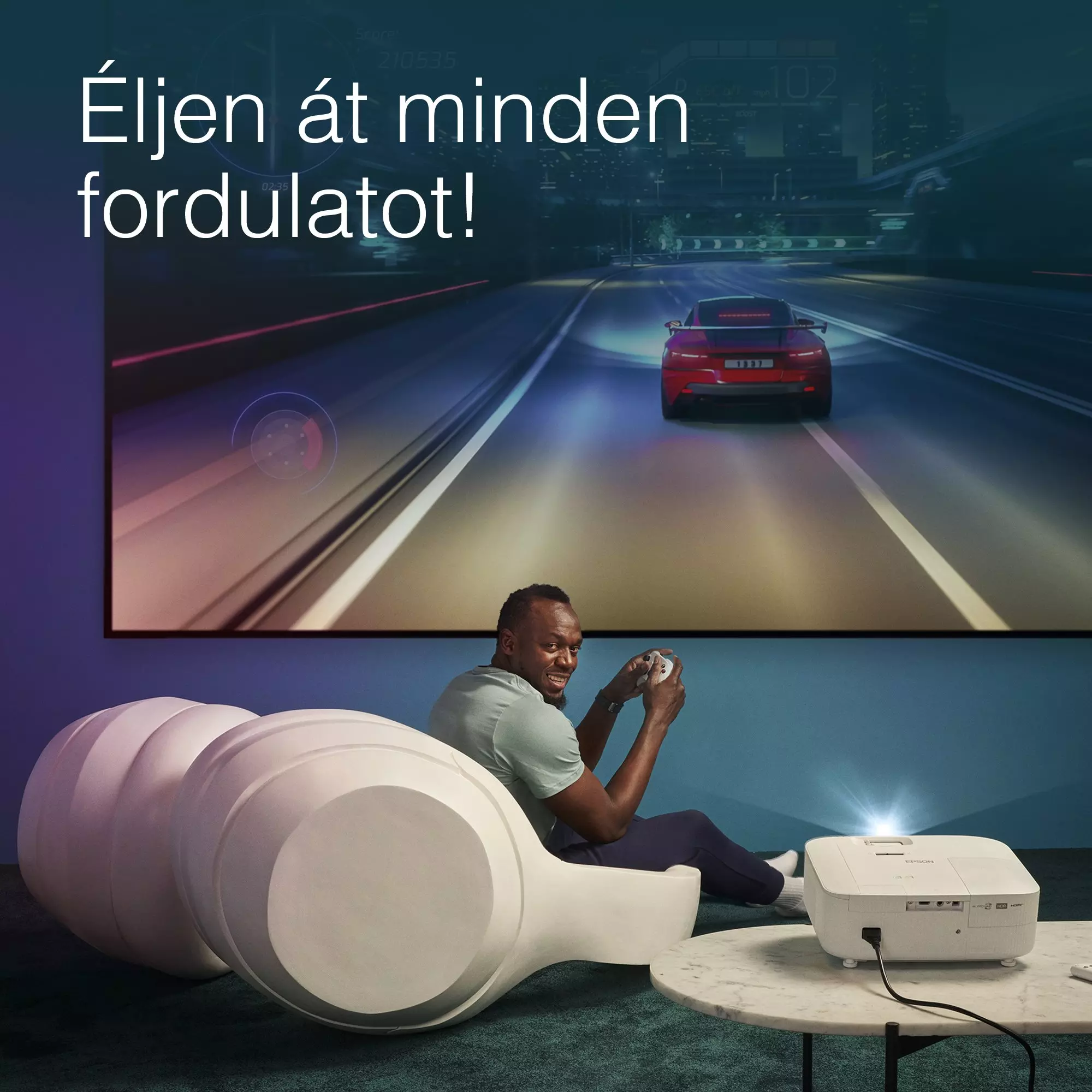 Férfi videojátékot játszik nagy képernyőn. Piros autó. Fehér szék és projektor előtérben.