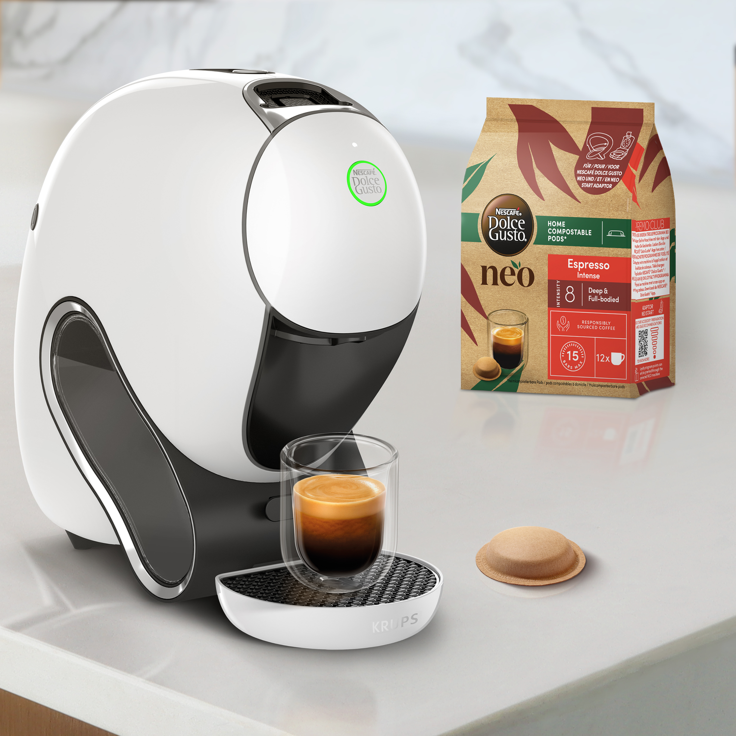 White and black coffee machine, a coffee cup, coffee pod and a bag of coffee pods are on a white surface.