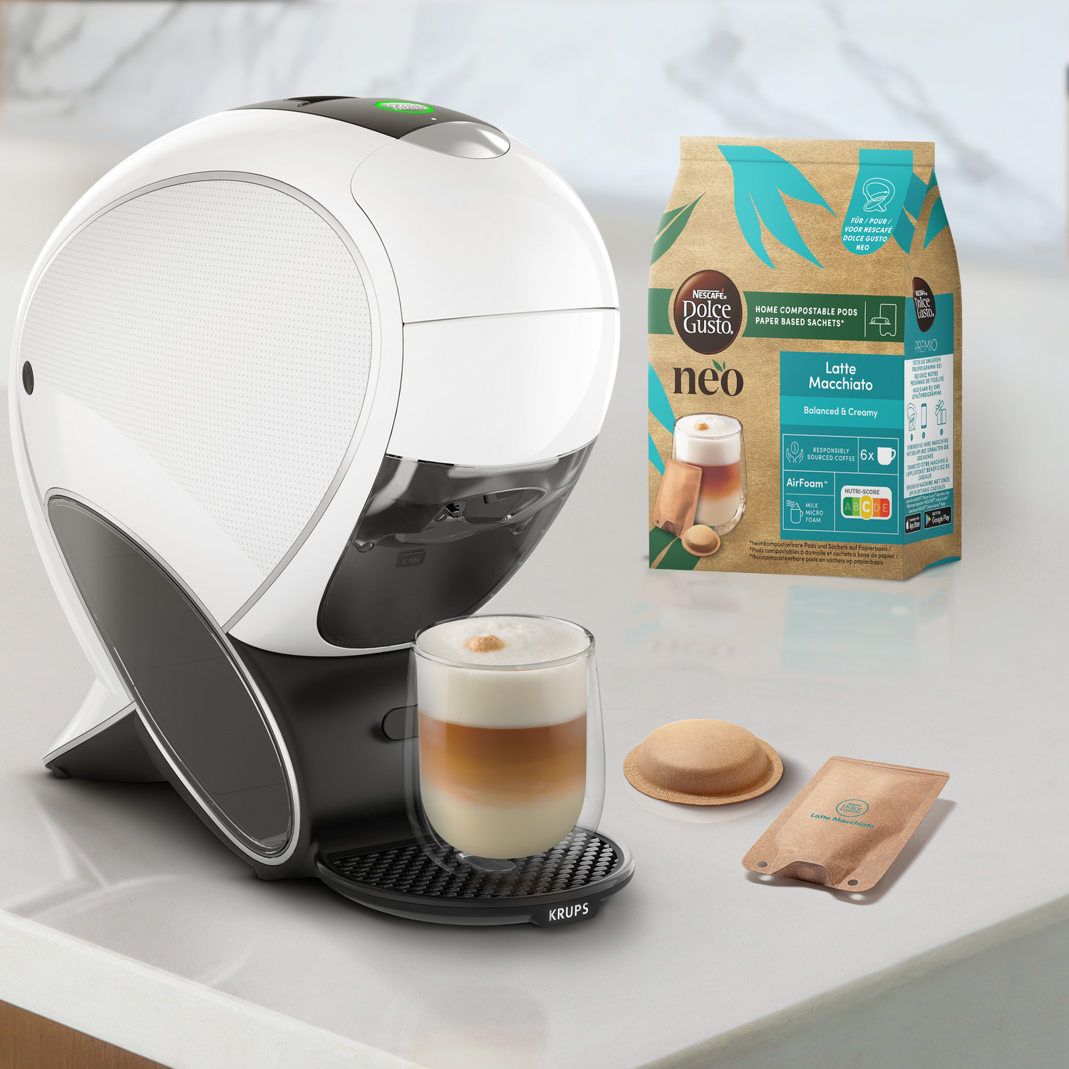 A white and black coffee machine with a latte macchiato and coffee pods on a white surface.