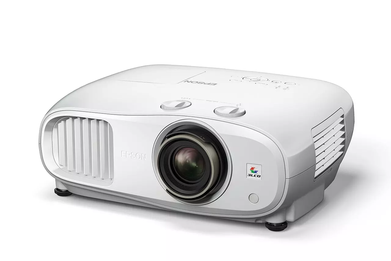 Egy fehér Epson projektor fehér felületen. Lencséje, vezérlőgombjai és szellőzőnyílásai vannak. Az Epson logó látható.