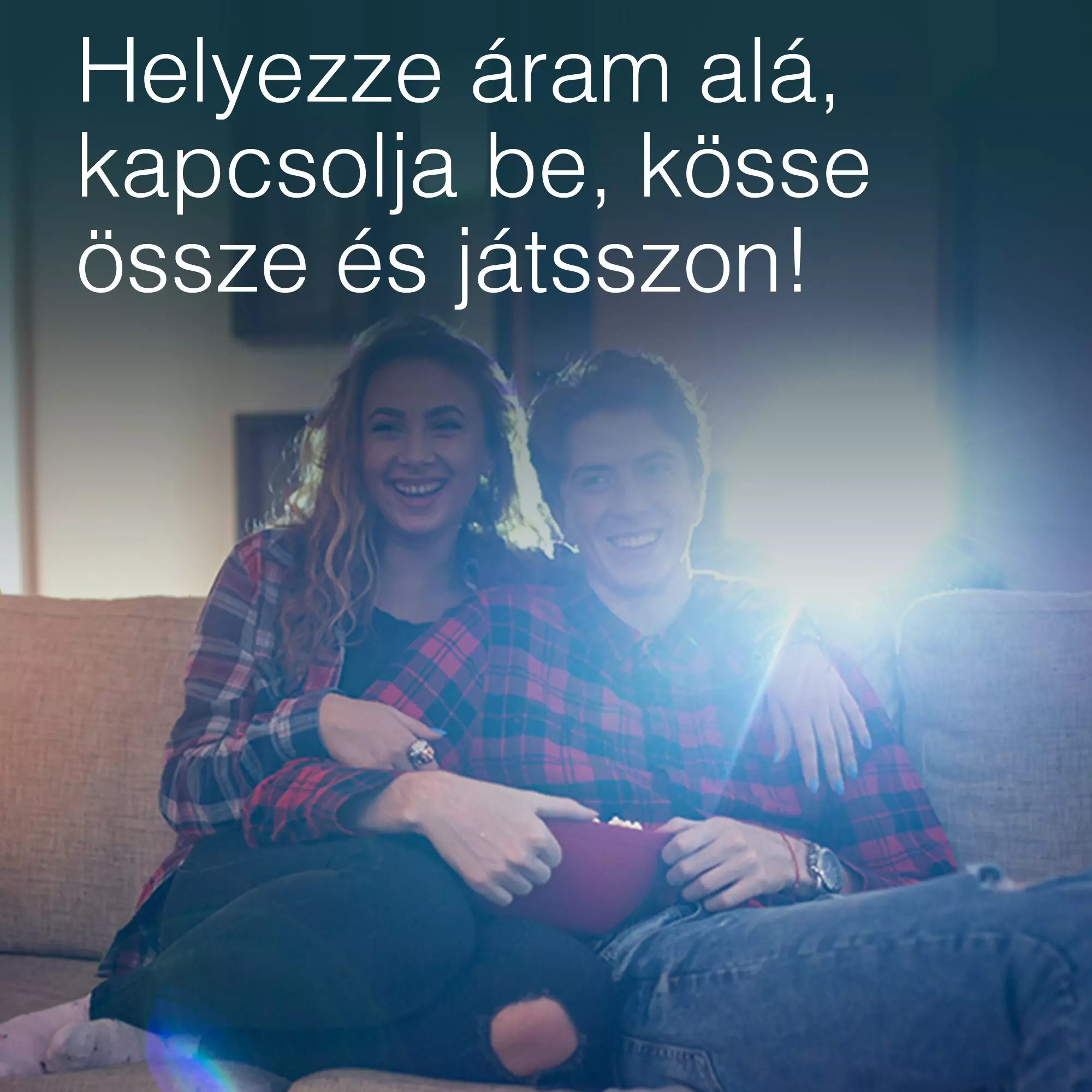 Egy mosolygó pár a kanapén, pattogatott kukoricát tartva. A nő kockás inget visel. A férfi farmernadrágot visel.