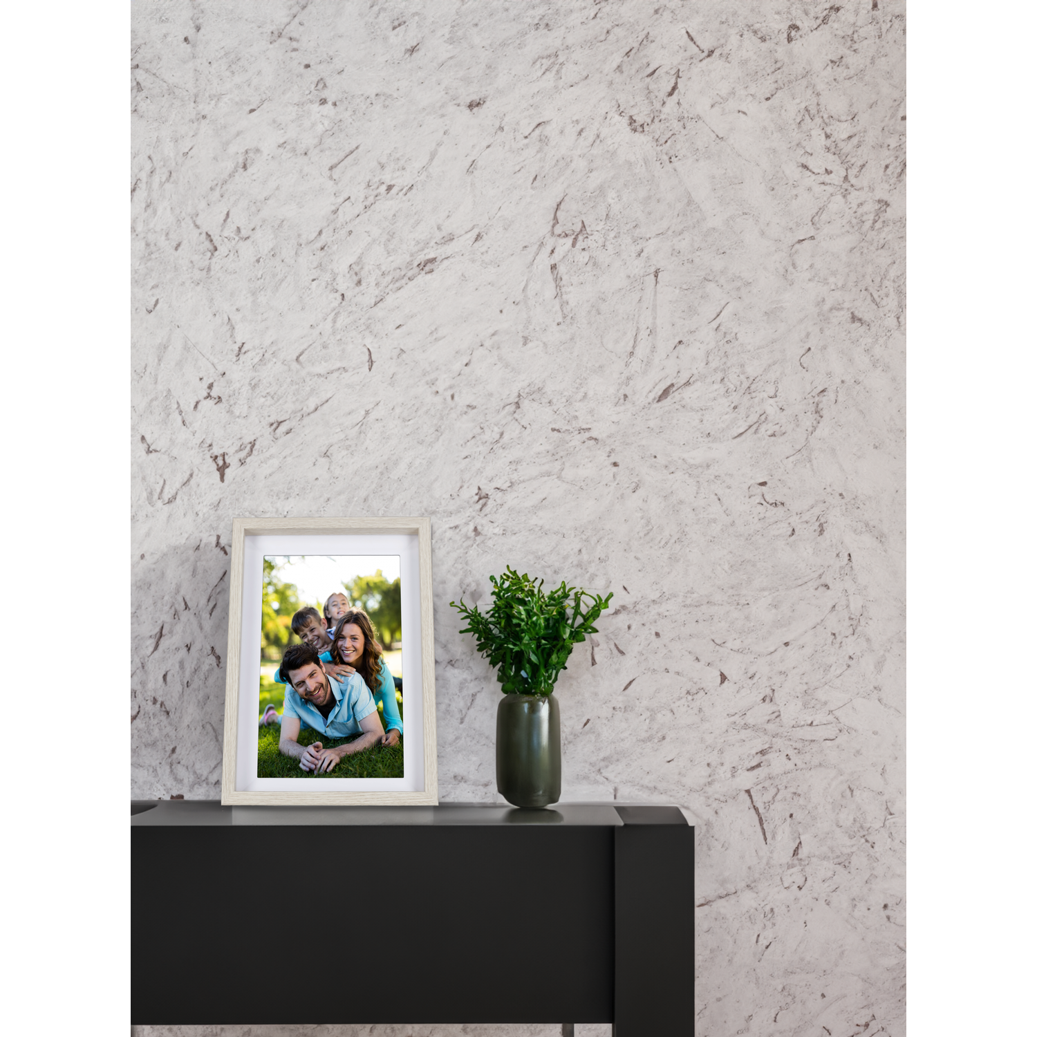 Une photo de famille encadrée sur une surface noire, plante verte dans un vase, contre un mur texturé.