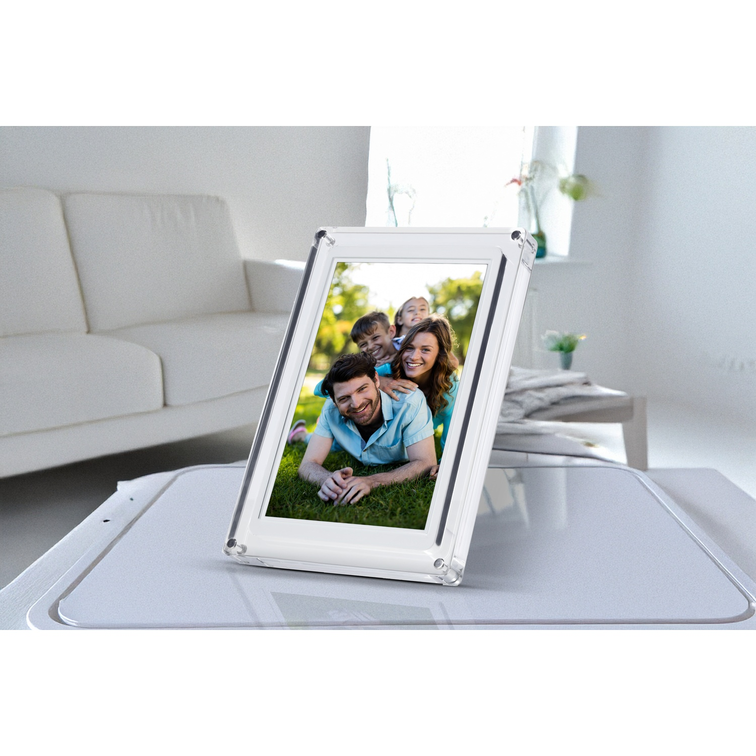 Un cadre photo transparent affiche une photo de famille. Un canapé et une table blancs sont en arrière-plan. La scène est intérieure, bien éclairée.