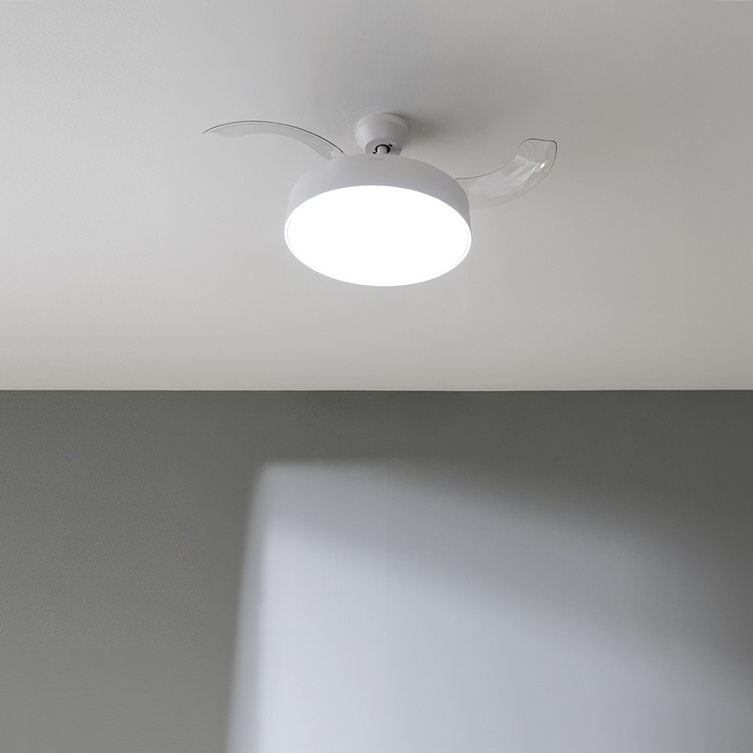 Un ventilador de techo blanco con una luz circular brillante en el centro. Dos aspas curvas y transparentes se extienden desde los lados.
