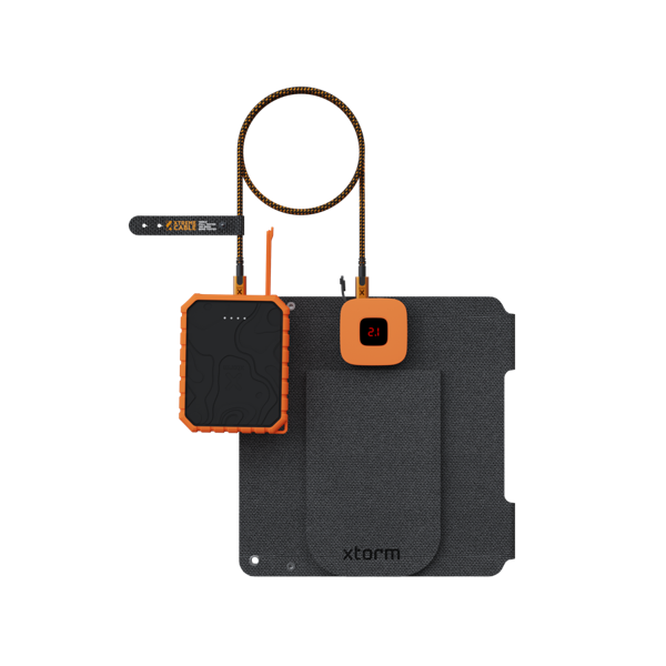 Dispositivos de carga naranjas y negros conectados a una estera gris oscuro. Cables, una pequeña pantalla y un banco de energía son visibles.