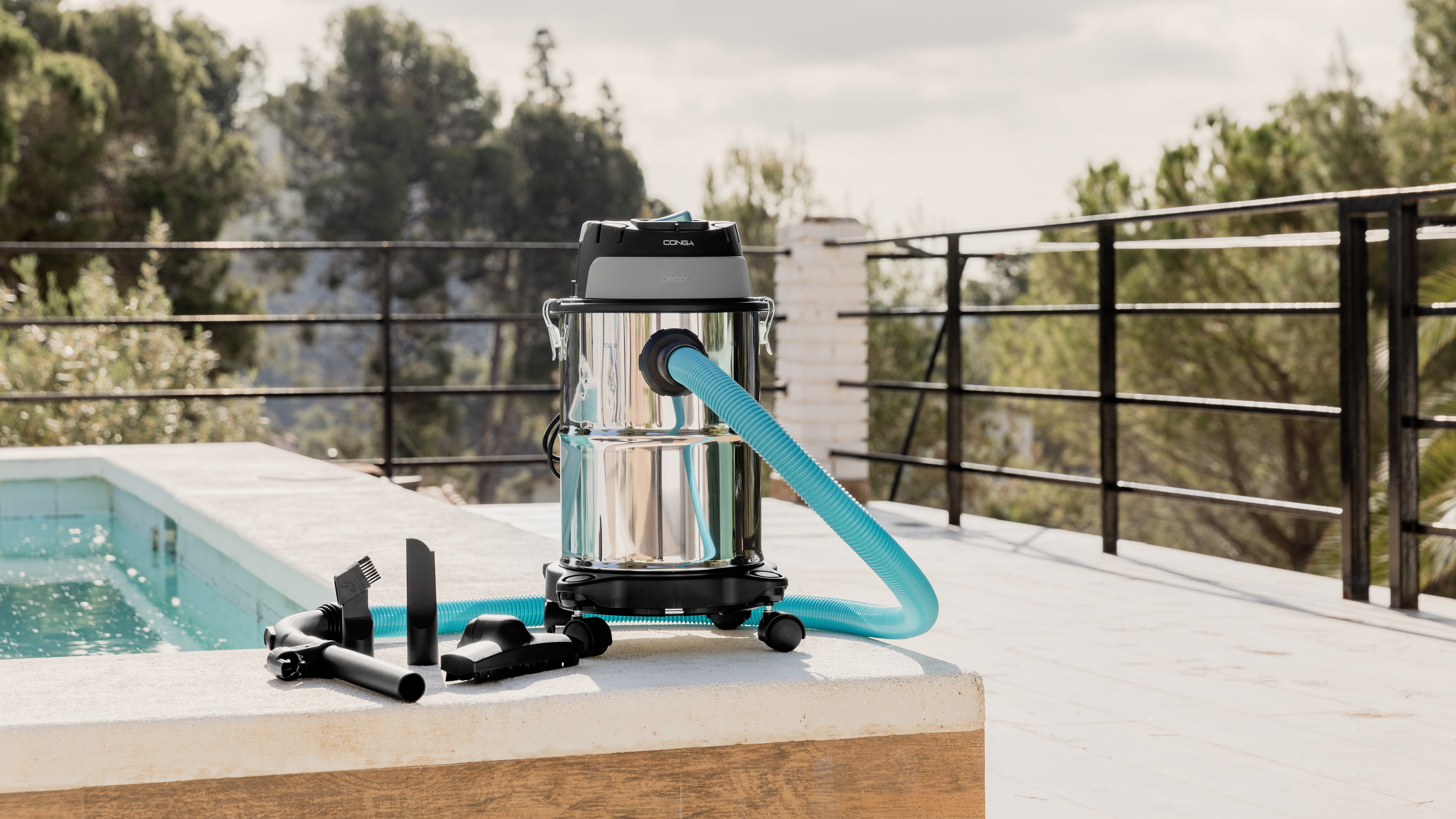 Una aspiradora en seco y húmedo con accesorios en una terraza. Al fondo, árboles y una piscina son visibles.