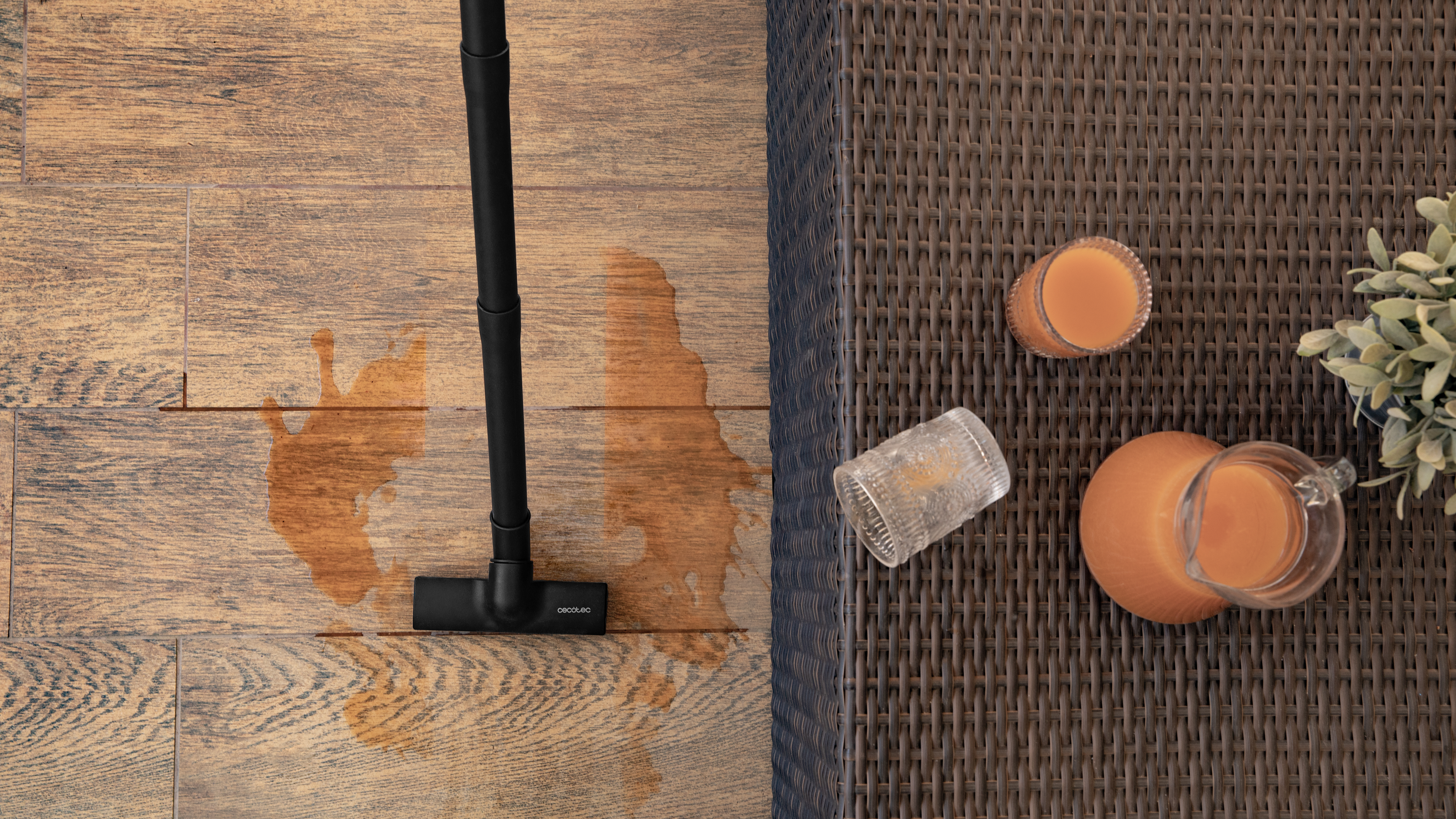 Líquido naranja derramado en suelo de madera con aspiradora. Mesa con jugo de naranja y plantas.