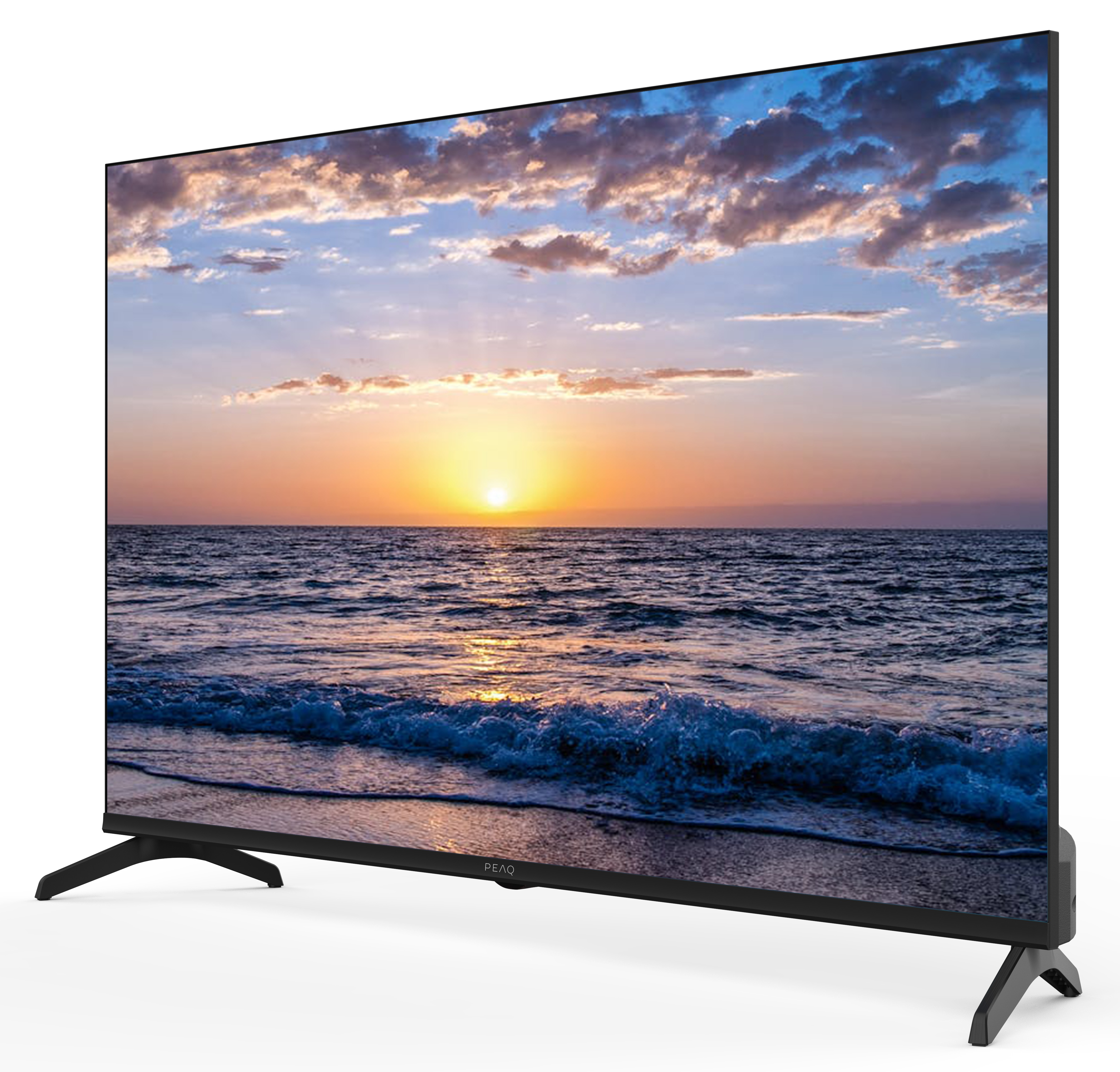 Telewizor wyświetla zachód słońca nad oceanem. Niebo jest niebieskie z chmurami. Fale rozbijają się o brzeg. Telewizor stoi na białej powierzchni.