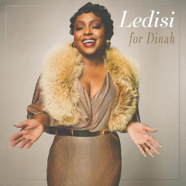 Ledisi in goldenem Kleid und Pelzstola, lächelnd, mit offenen Armen. Text: 'Ledisi for Dinah' auf hellem Hintergrund.