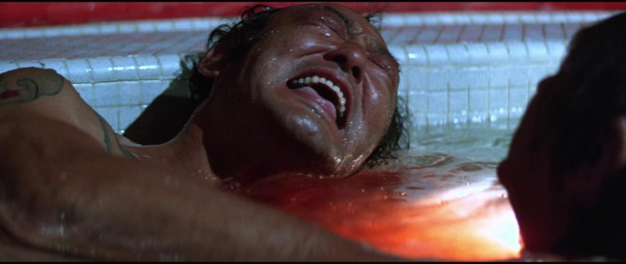 Das Gesicht eines Mannes schreit im Wasser. Blut ist im Wasser sichtbar. Auf seinem Arm befindet sich ein Tattoo.