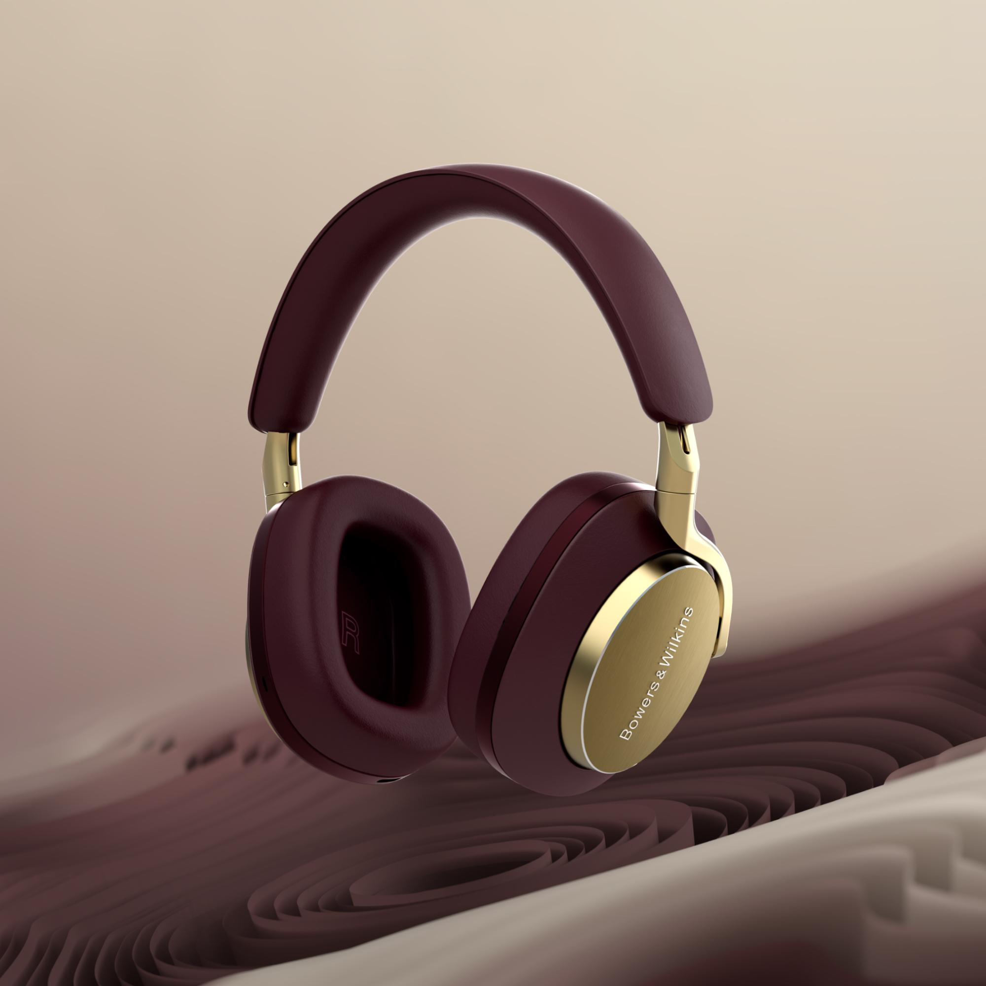Burgunderfarbene Kopfhörer mit goldenen Akzenten schweben vor einem wellenförmigen braunen Hintergrund. Bowers & Wilkins Logo ist sichtbar.