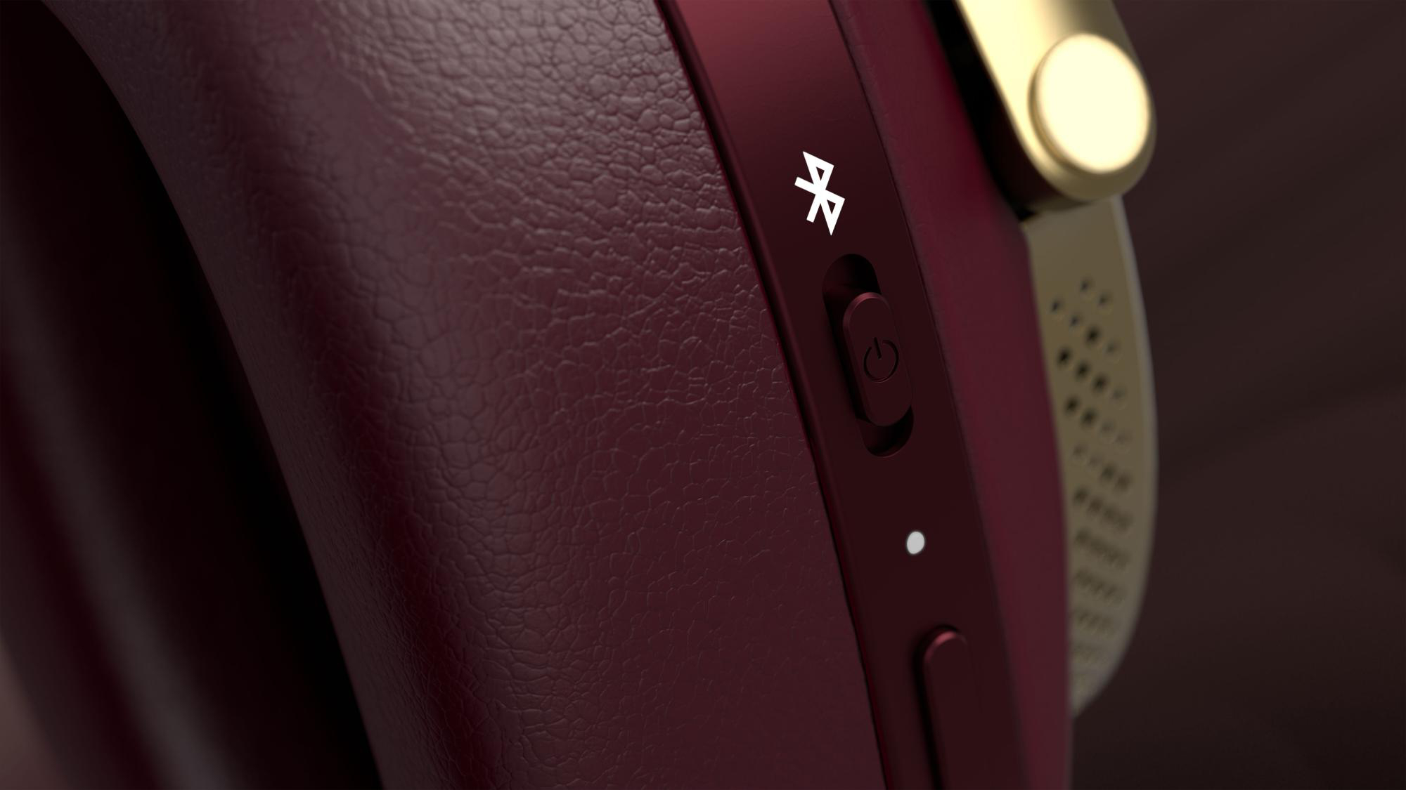 Nahaufnahme eines roten Kopfhörers. Goldakzente und ein Bluetooth-Symbol sind sichtbar. Ein-/Aus- und andere Steuertasten sind vorhanden.