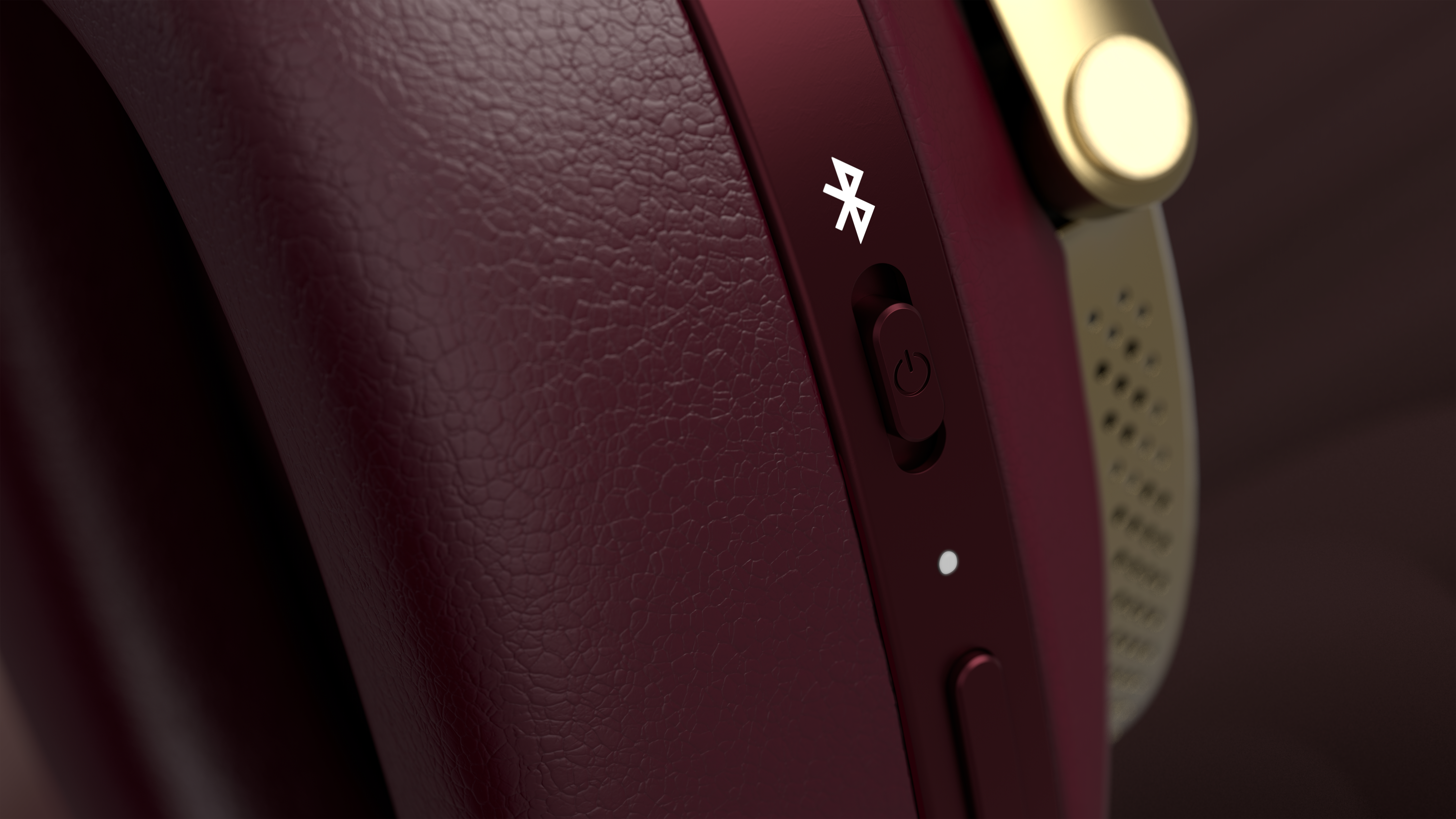 Nahaufnahme eines weinroten Kopfhörers. Ein Power-Knopf, Bluetooth-Symbol und ein weißes Licht sind sichtbar.