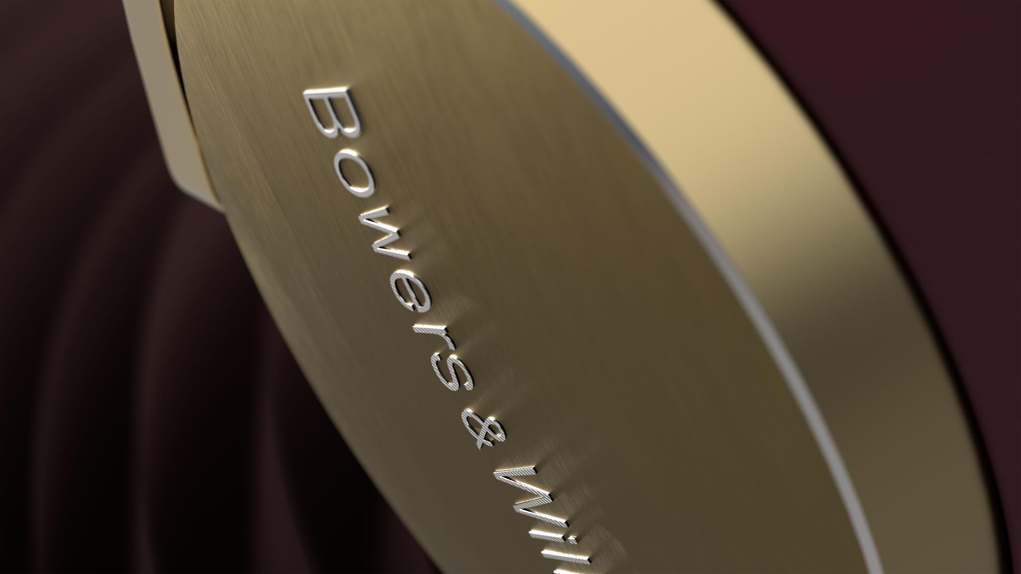 Nahaufnahme einer goldfarbenen Oberfläche mit silberner Aufschrift 'Bowers & Wilkins'. Der Hintergrund ist dunkelburgunderfarben.
