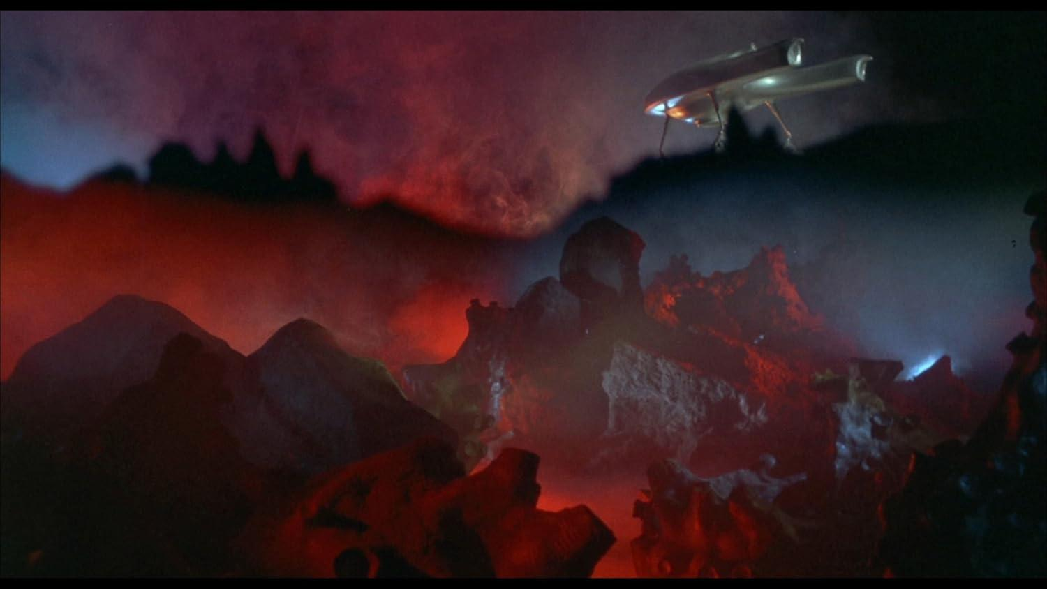 Ein Raumschiff fliegt über einer felsigen Landschaft. Rote und dunkle Wolken füllen den Himmel. Die Szene hat eine dramatische und bedrohliche Atmosphäre.