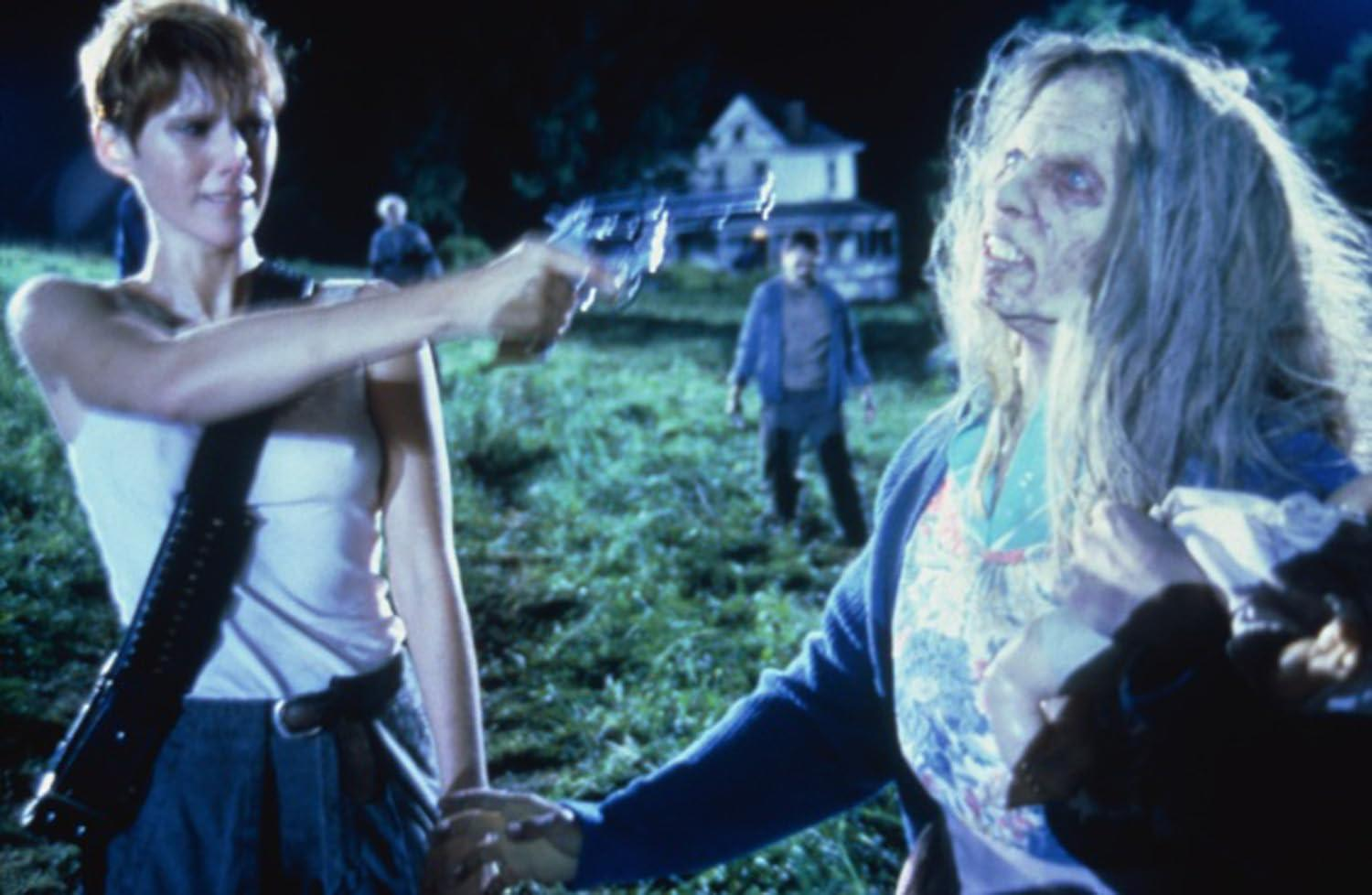 Eine Frau zielt mit einer Pistole auf einen Zombie. Ein anderer Zombie und ein Haus befinden sich im Hintergrund. Die Szene ist dunkel und im Freien.