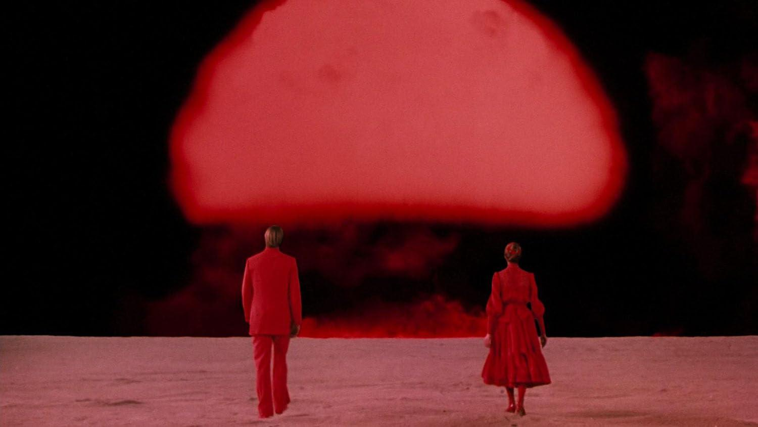Zwei Personen in roten Anzügen gehen auf eine große rote Wolke vor schwarzem Himmel zu. Der Boden ist blassrot.