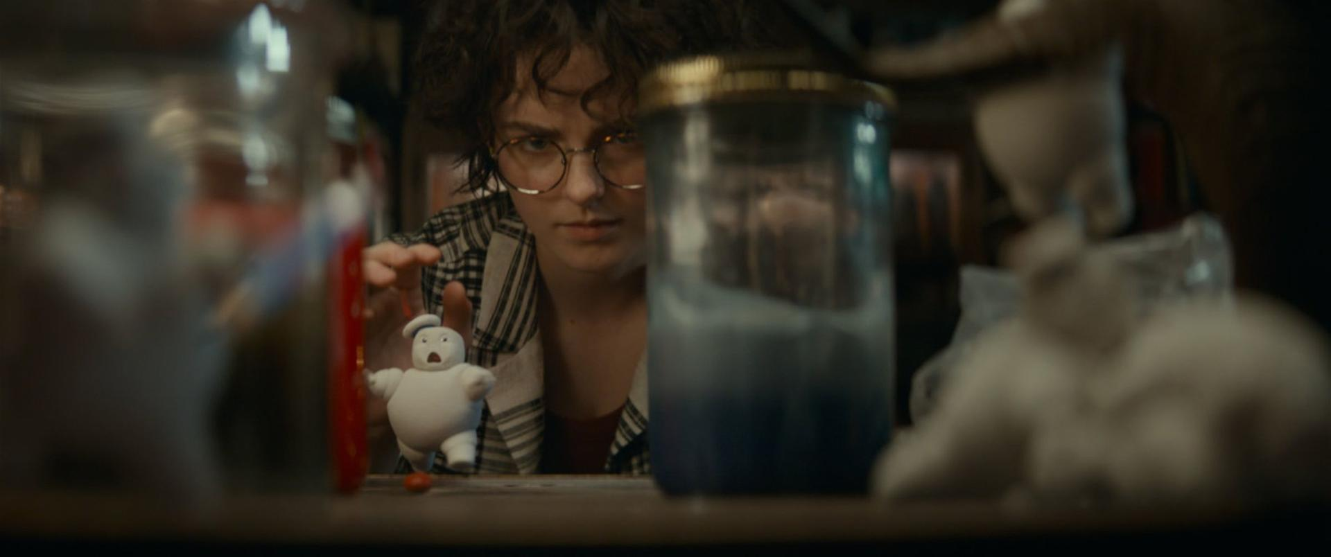 Eine Person mit Brille betrachtet ein Stay Puft Marshmallow Man-Spielzeug. Gläser und andere Gegenstände sind vor und hinter der Person.