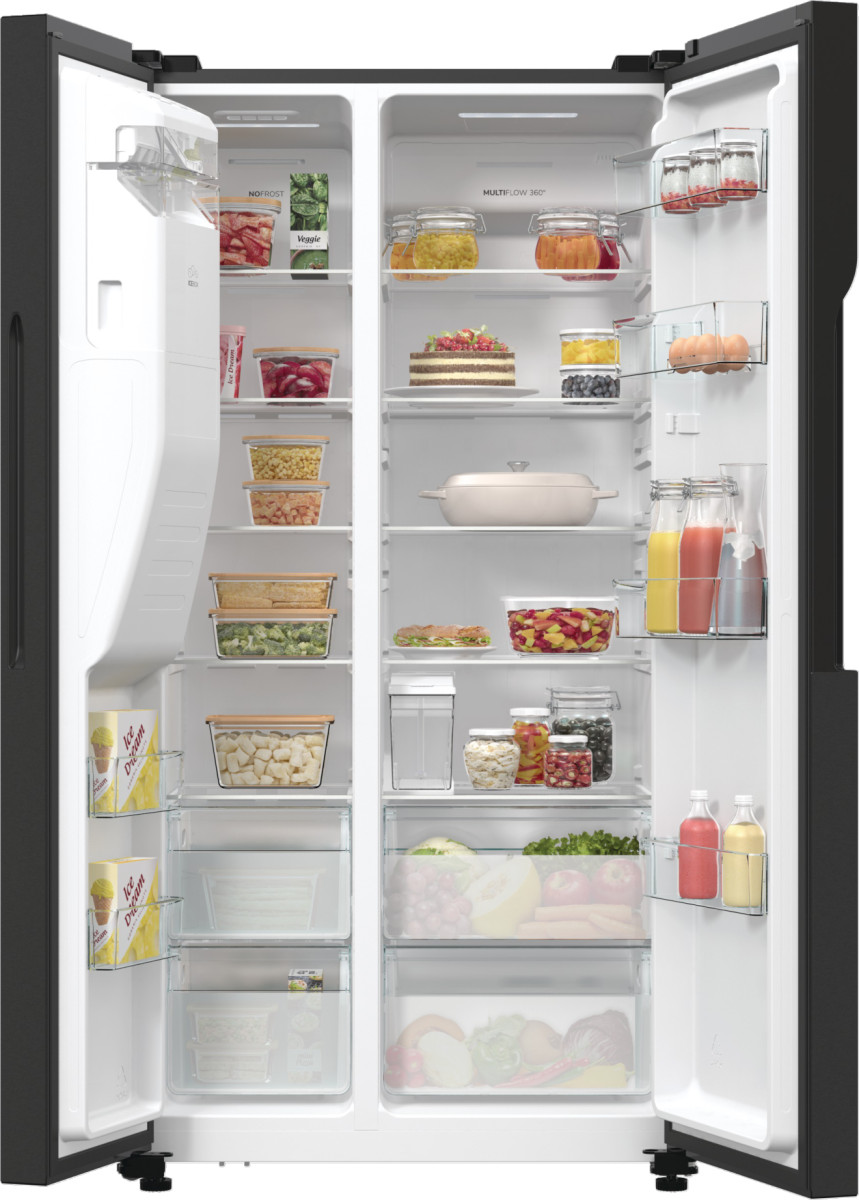 Otwarta lodówka wypełniona produktami spożywczymi, takimi jak owoce, warzywa, słoiki, napoje i ciasto, wszystko starannie ułożone.