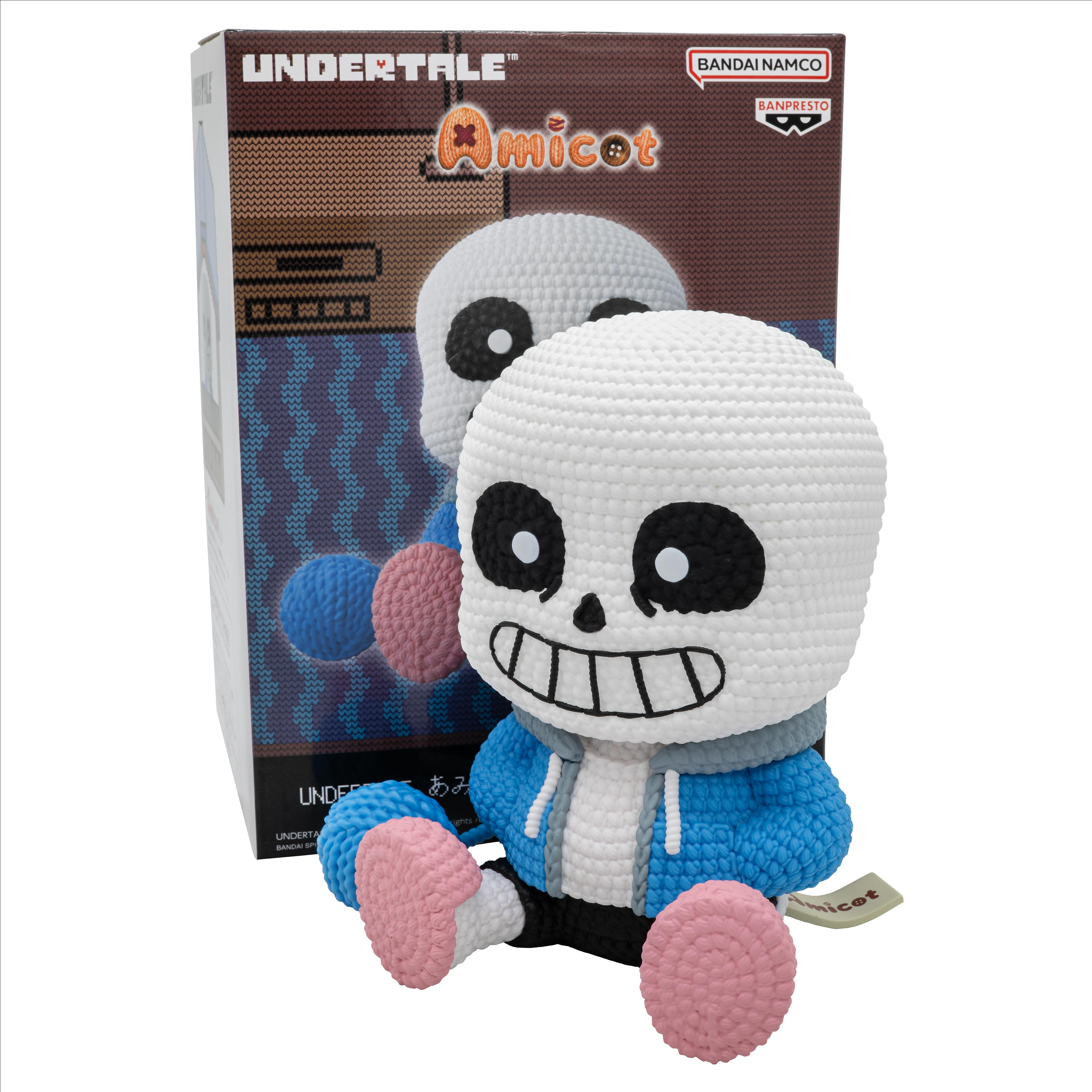 Un juguete de Sans tejido de Undertale, con una caja en el fondo. El juguete es blanco, azul y rosa.