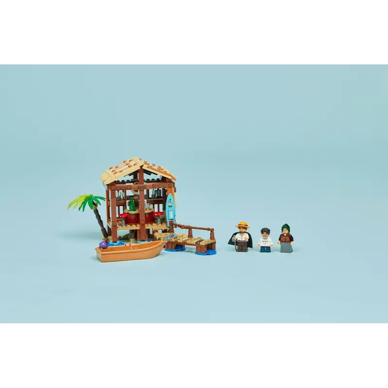 Una scena Lego sulla spiaggia con un bar, una barca e tre personaggi. Il bar ha un tetto di paglia, una tavola da surf e una palma.