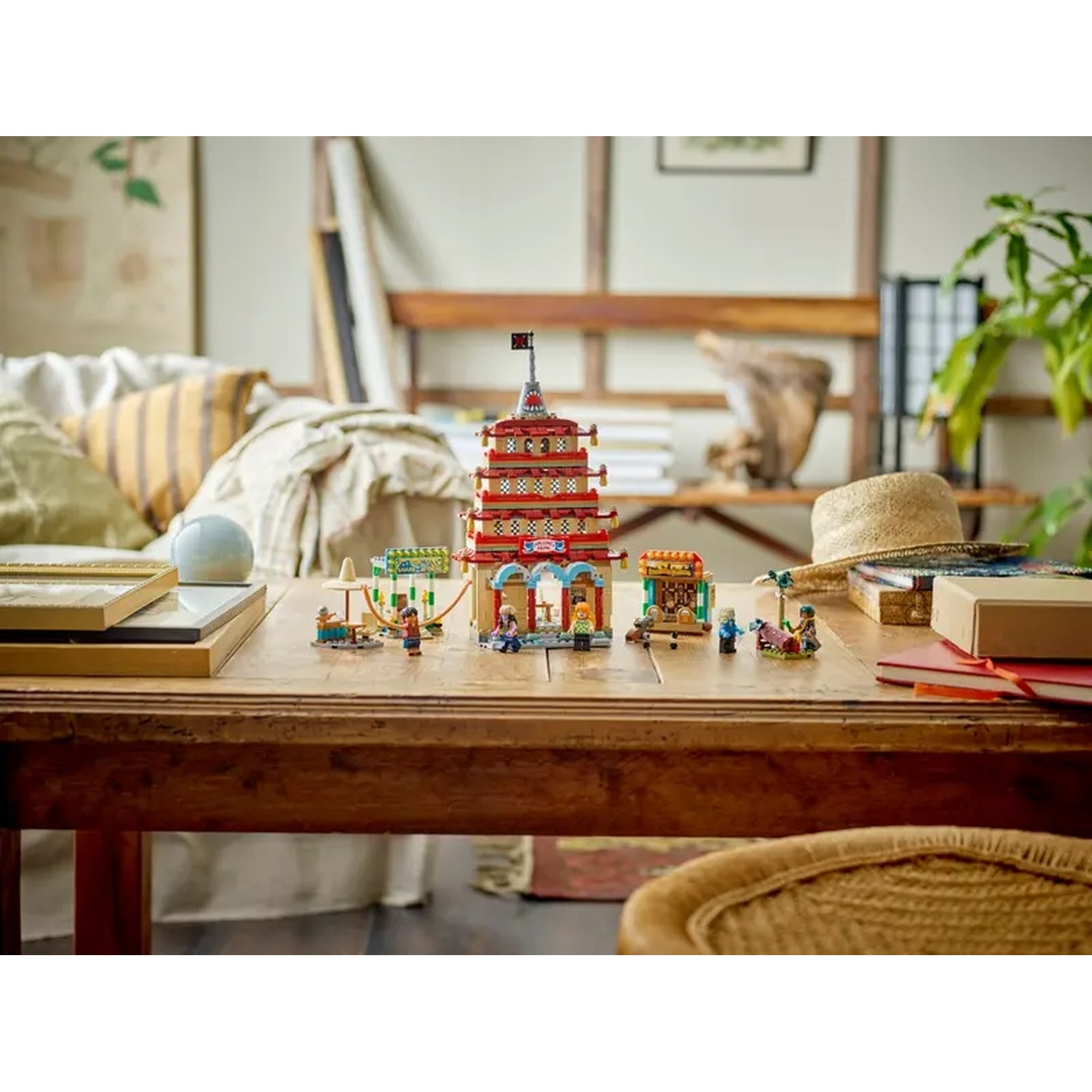 Un tavolo di legno con un set Lego di una pagoda rossa e bancarelle del mercato. Ci sono personaggi Lego e un cappello di paglia sullo sfondo.