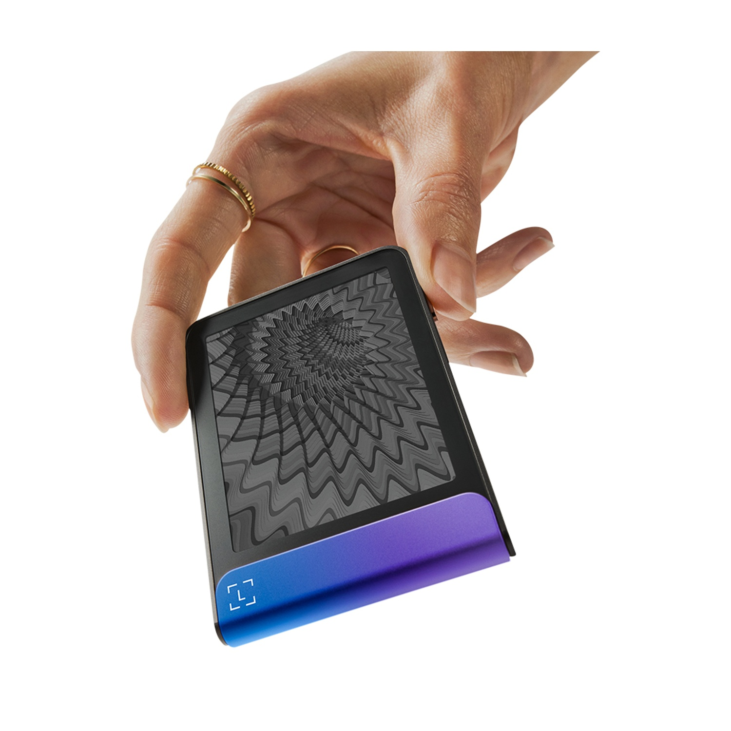 Una mano tiene in mano un dispositivo nero e blu con uno schermo a motivi. La mano ha degli anelli. Lo sfondo è bianco.