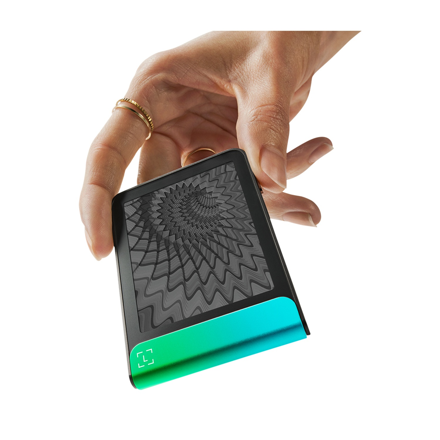Una mano tiene in mano un dispositivo nero con una base verde-azzurro sfumata. Lo schermo ha un motivo grigio a spirale. Anelli sulle dita.