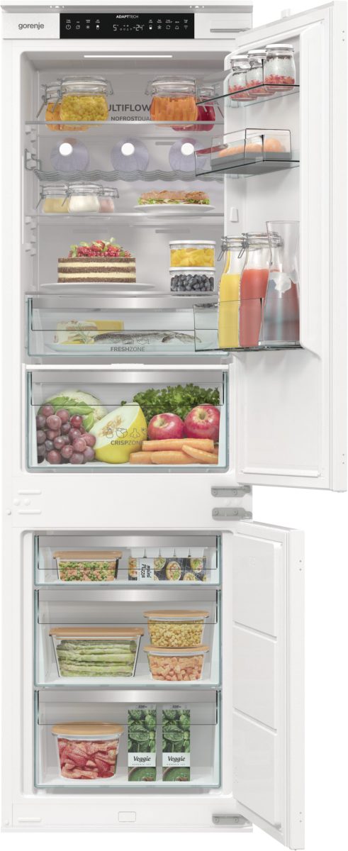 Otwarta lodówka z jedzeniem. Widoczne słoiki, owoce, warzywa, ciasto i napoje.